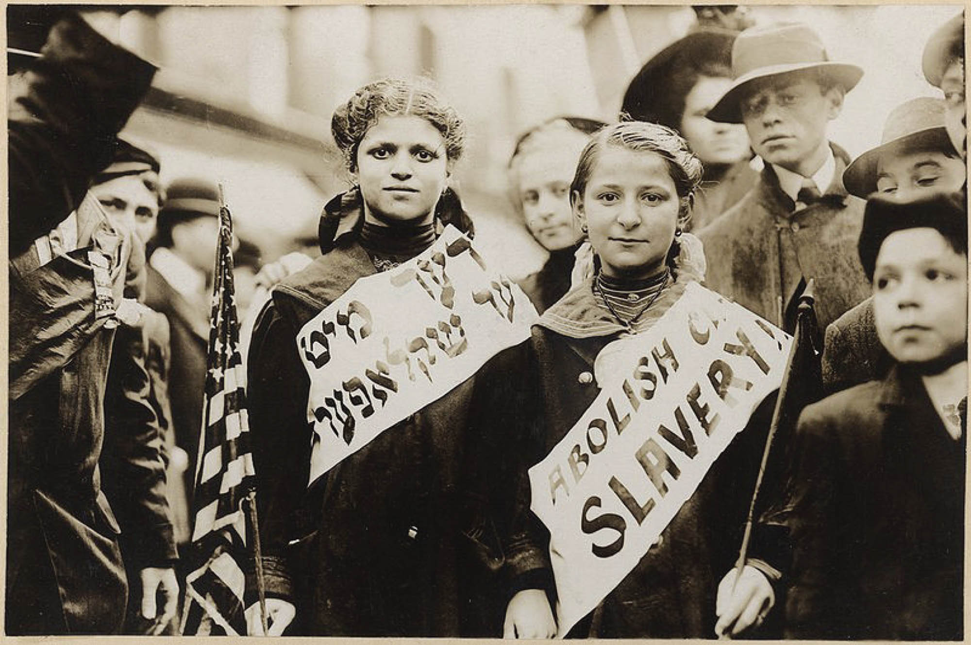 Photo of two young girls wearing a sash with the slogan “Abolish child slavery” written in both English and Yiddish.