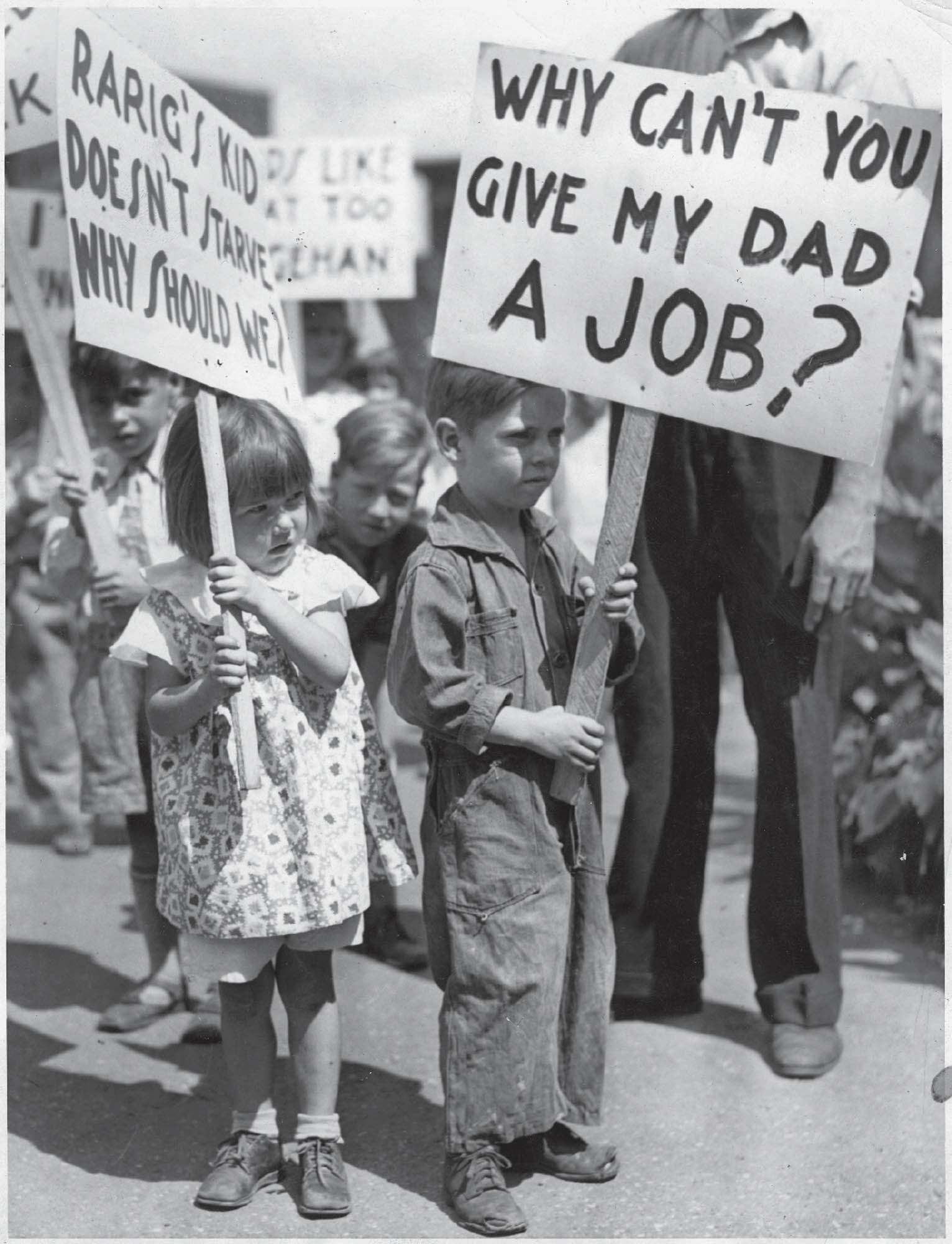 Black and white photograph of a man with his children, who hold signs protesting unemployment.