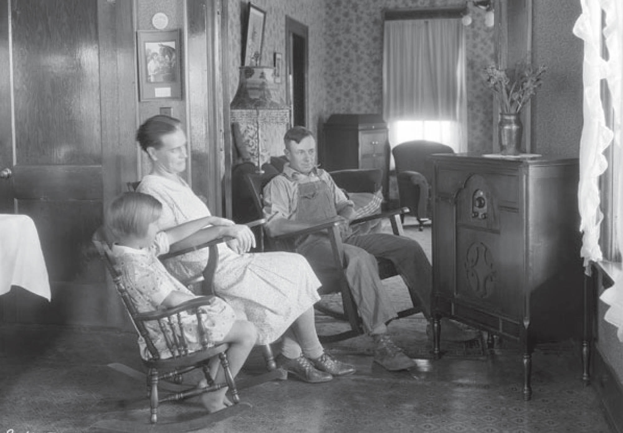 A family sits in rocking chairs listening to a radio broadcast in 1930.