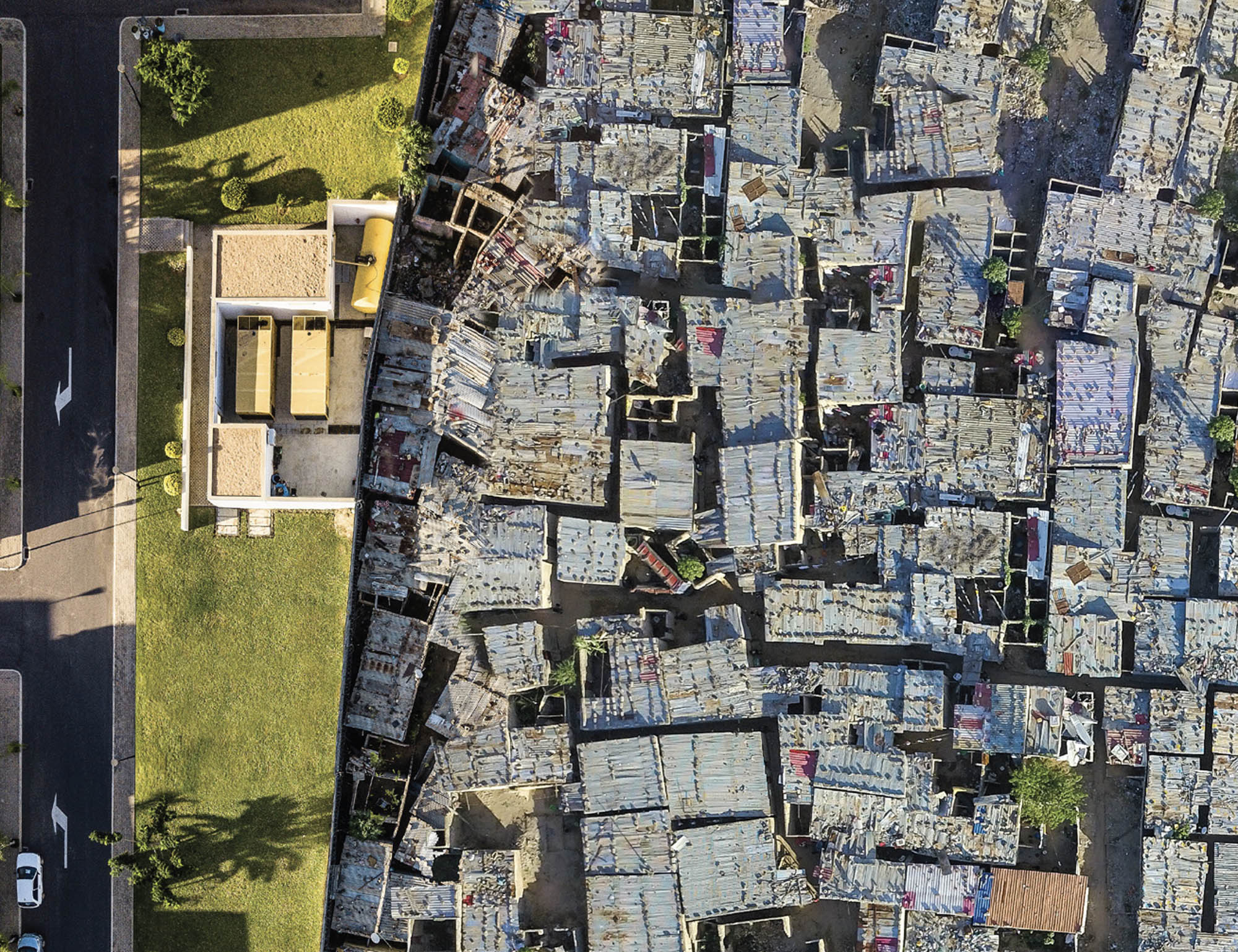 Aerial photo of two bordering neighborhoods in Luanda, Angola. The neighborhood on the left has larger houses that are spaced out and have nice amenities such as a pool and a backyard. The neighborhood on the right contains smaller houses that are packed together and built on dirt.