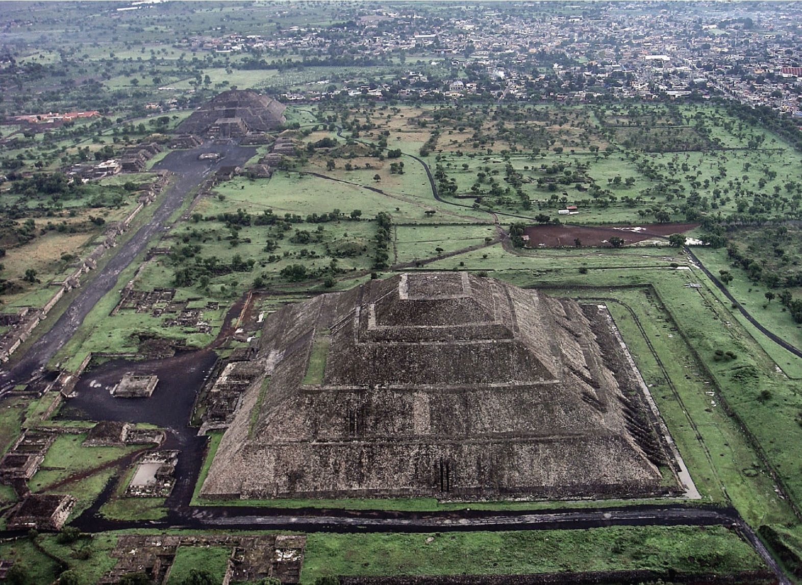 Birds-eye photo of Teotihuacan shows the city’s two largest structures. Both are pyramid-shaped, tall, and there is a road connecting the two structures.