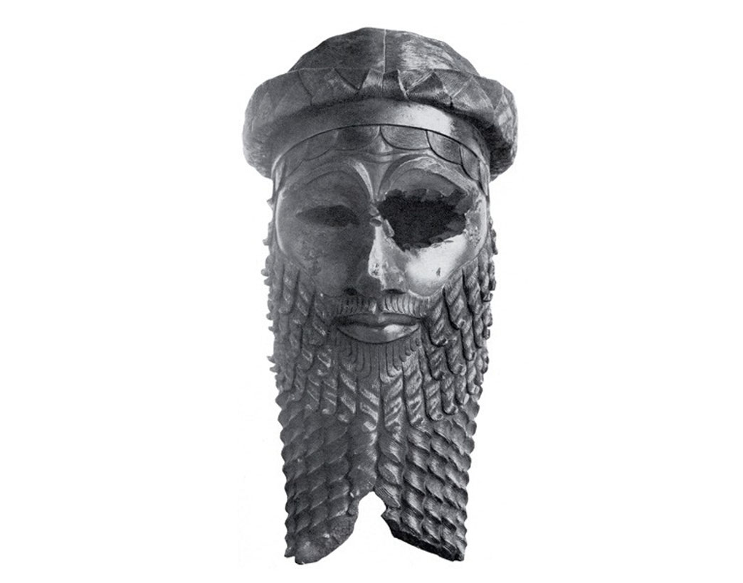 Bronze sculpted head of an Akkadian emperor featuring a very detailed carved beard and hat. One eye is missing from the sculpture, probably a result of age decay.