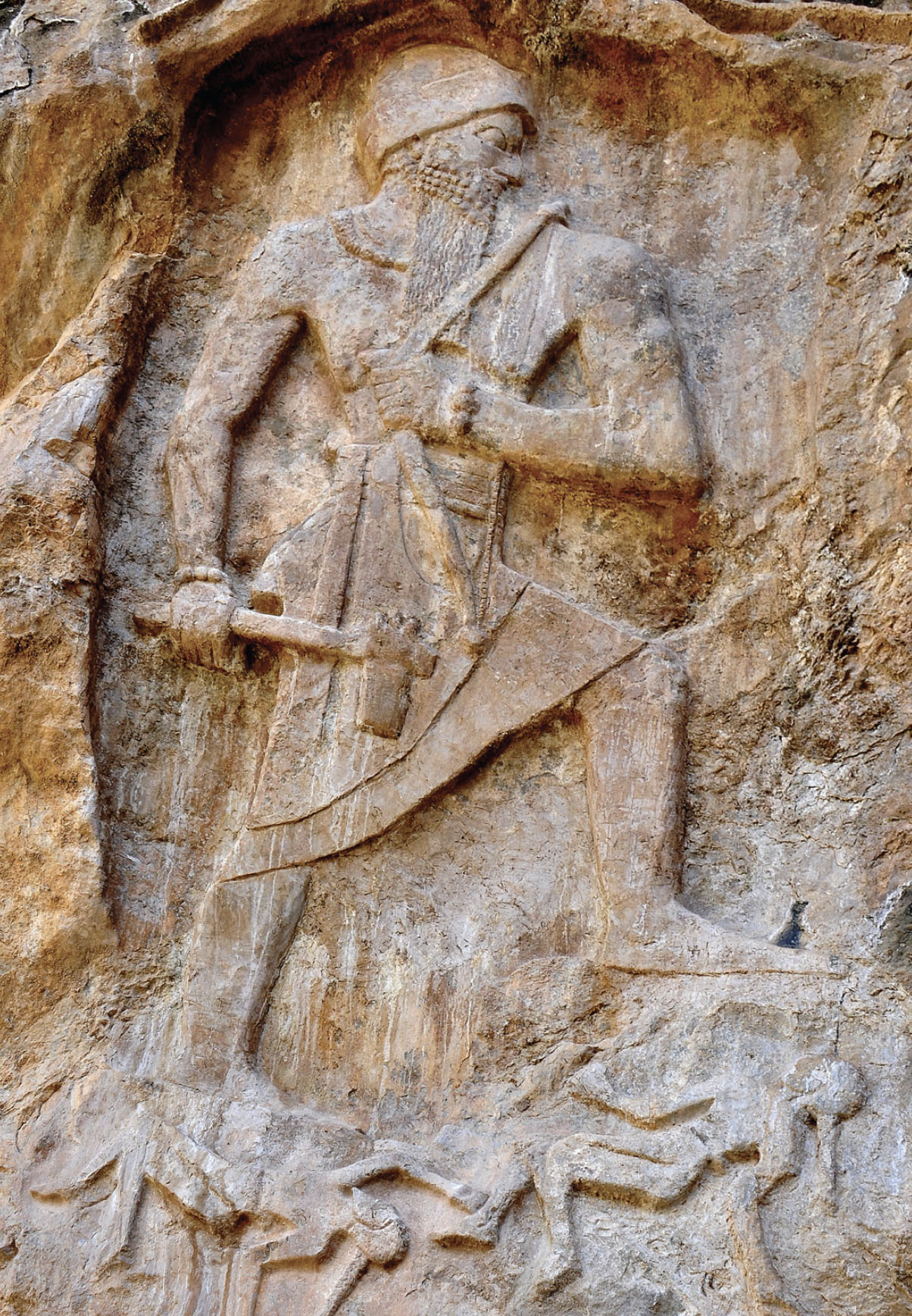 Carved rock depiction of a very large man stomping on much smaller people