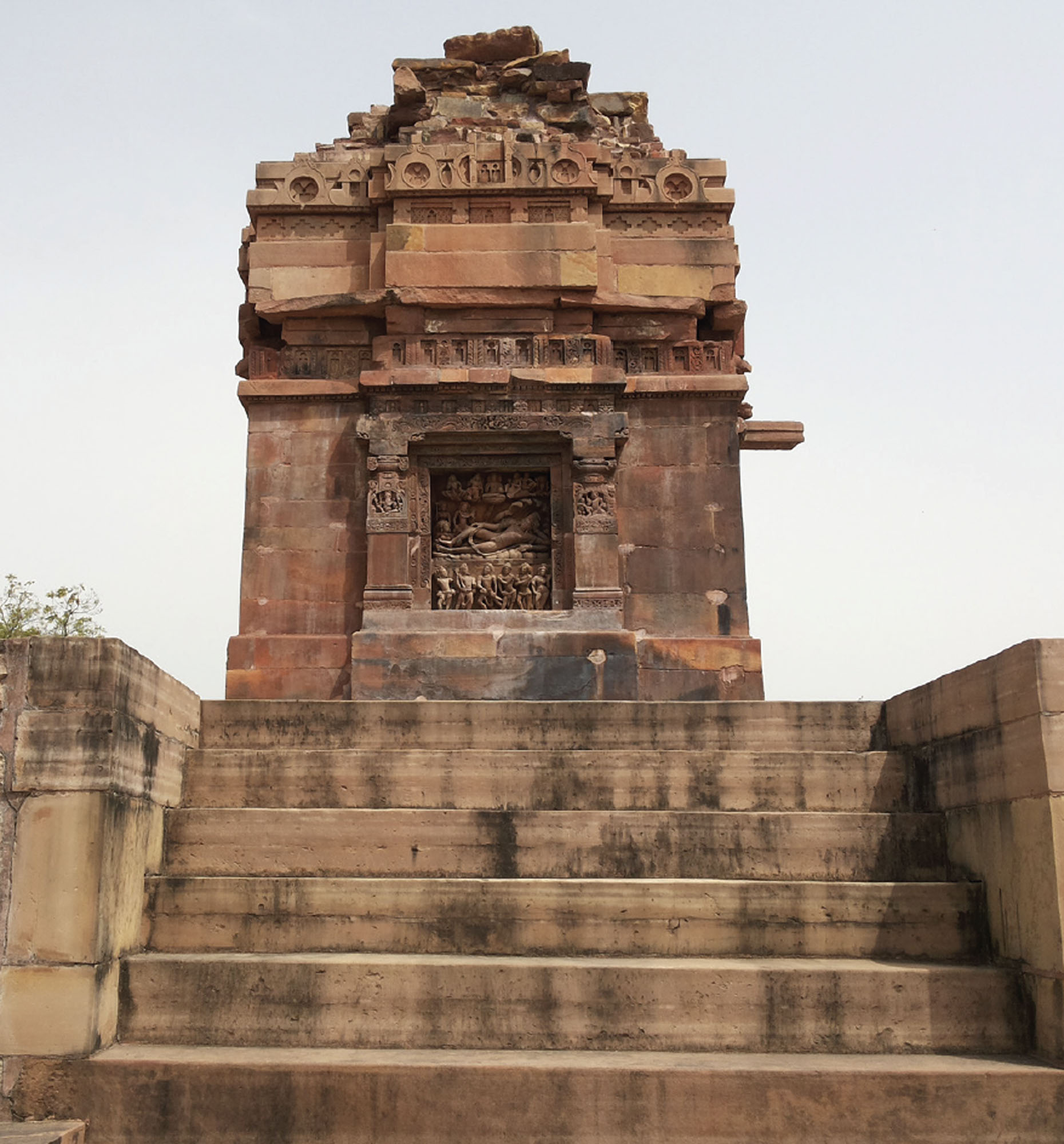 A small, ancient stone temple. The temple rests at the top of a set of stairs. 