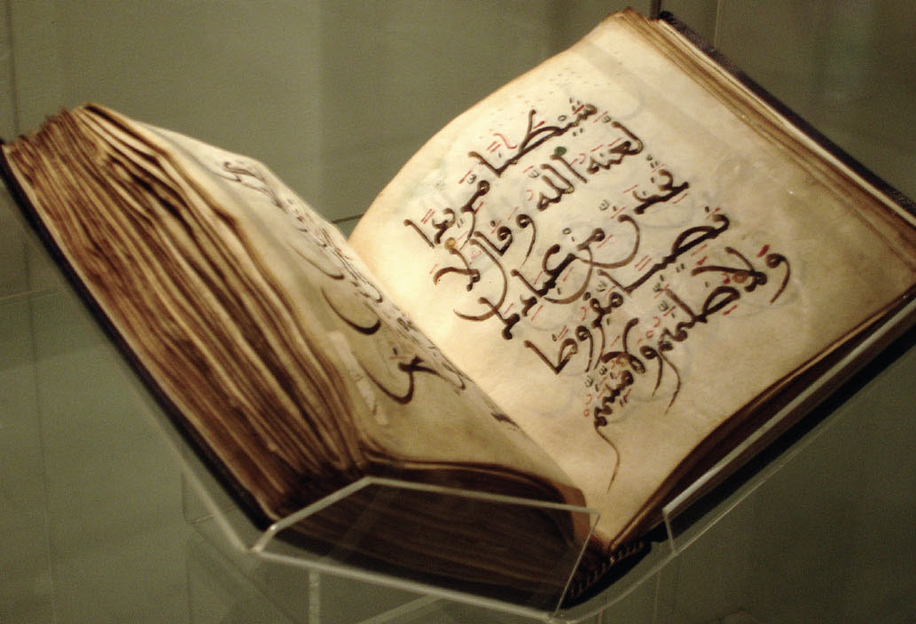 Picture of a book, held open in a museum display case, featuring Arabic script