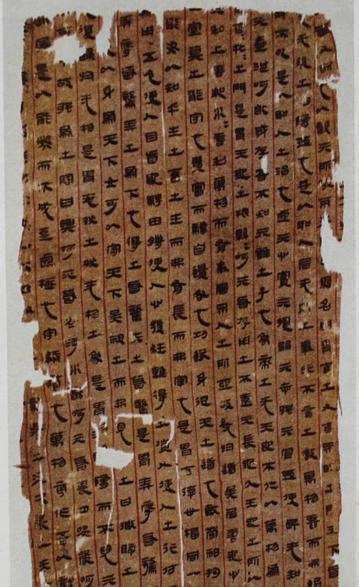 Picture shows a manuscript covered in language symbols, written in black ink, on a piece of brown silk