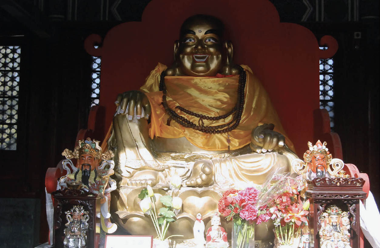 A photo of a golden sculpted smiling Buddha surrounded by flowers and gifts 