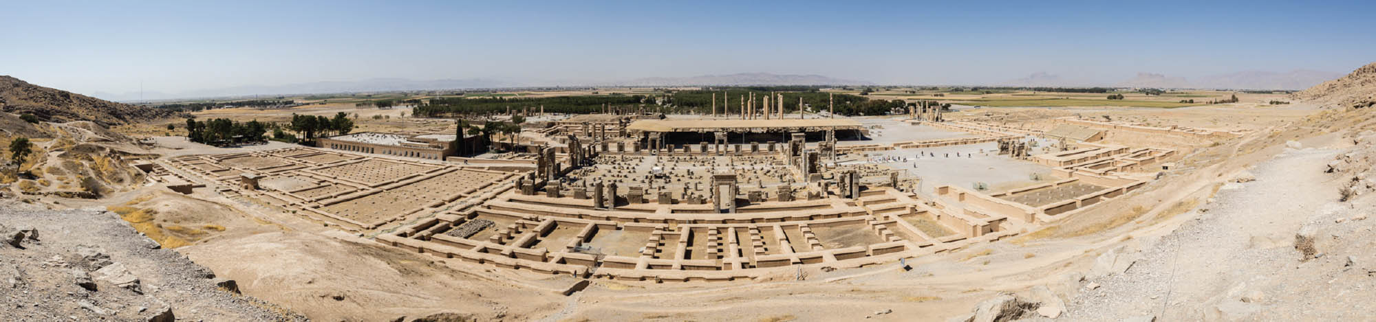 A panoramic photograph of what remains of Persepolis. Some structures remain, mostly broken or partially burned. 