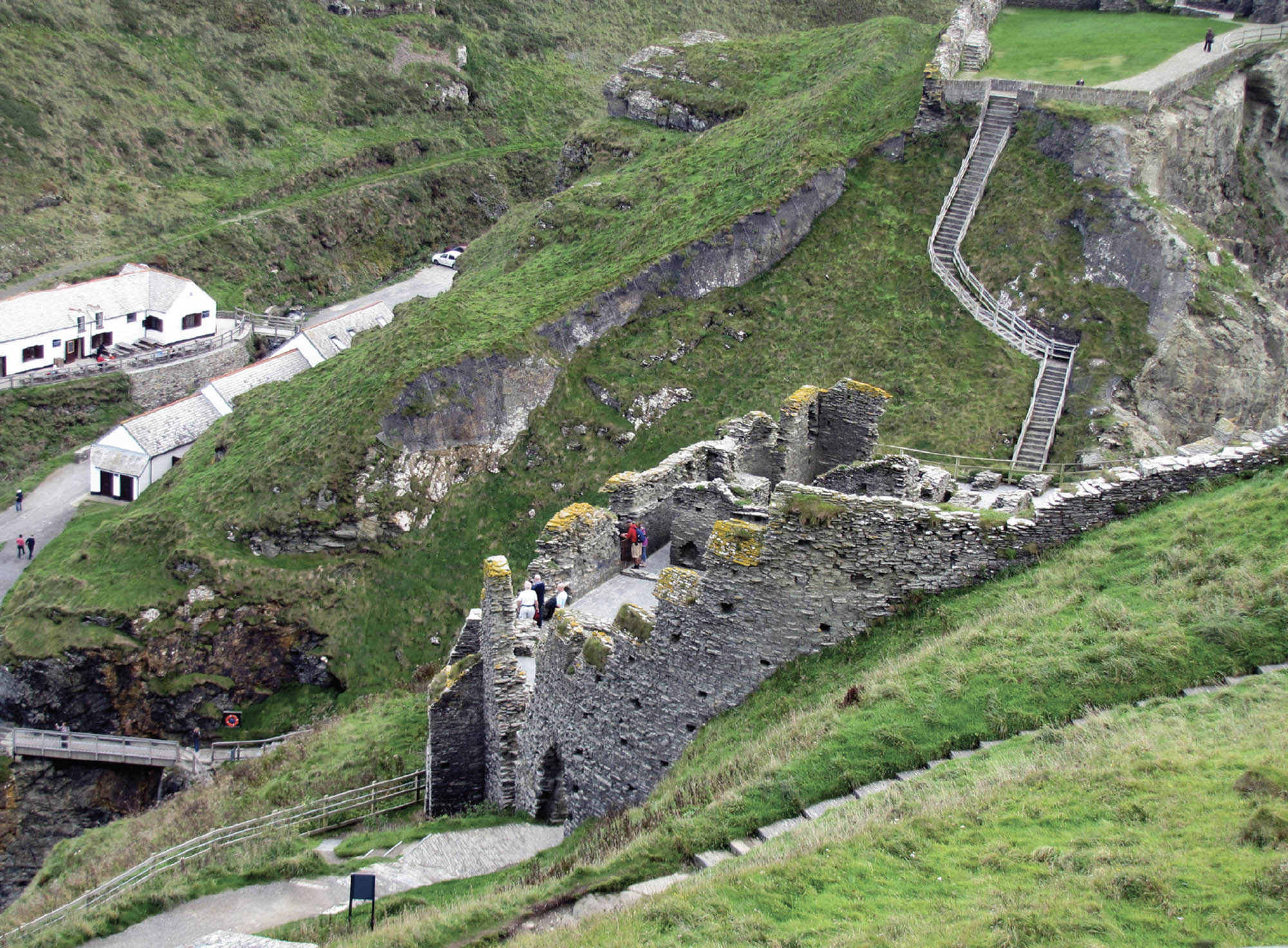 Photo of remains of a stone castle on a green hillside. A long, winding staircase leads up to the castle.