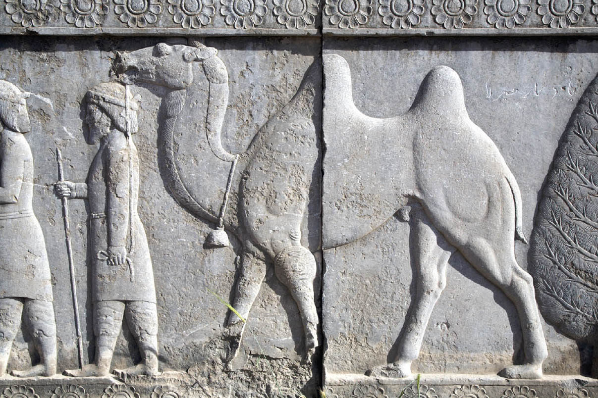 Stone carving of a camel walking behind two travelers.