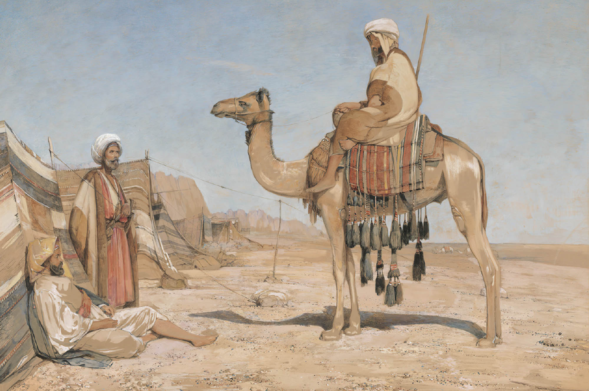 A caravan guide dressed in a white tunic and headcloth sits on top of a camel.
