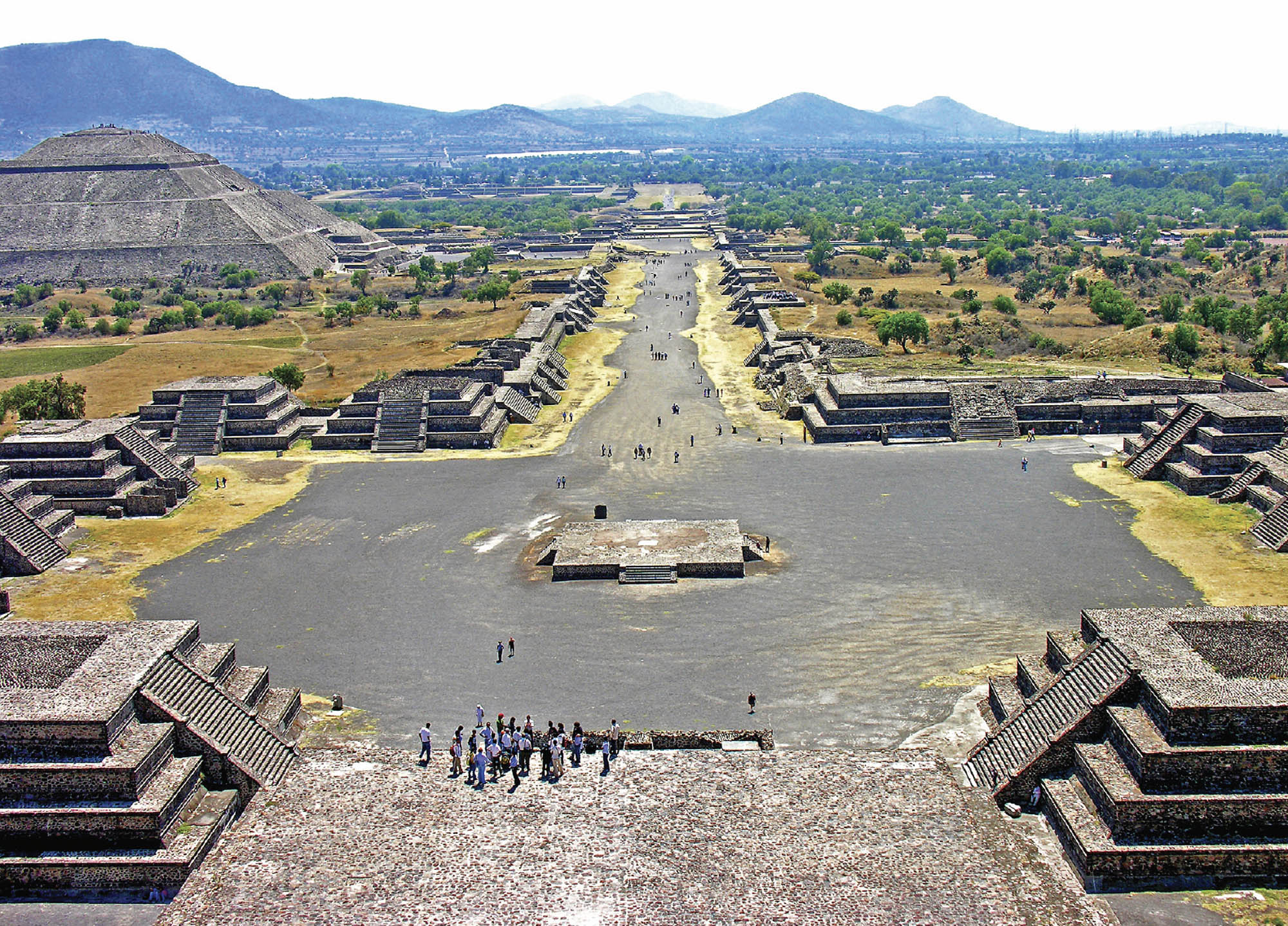 Birds-eye view of Teotihuacan showcasing the road that runs through the city, with many impressive pyramid-like structures surrounding.
