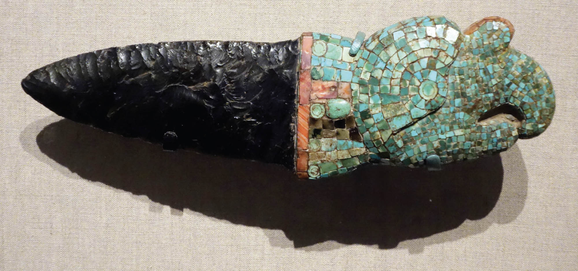 A knife carved from obsidian, a black, shiny rock. The handle is covered in a turquoise mosaic.