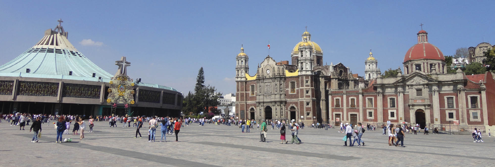 Photograph of tourists viewing great historical buildings. A rounded building with a turquoise-colored roof is on one side, and on the other side is a great cathedral topped in gold and red domes.