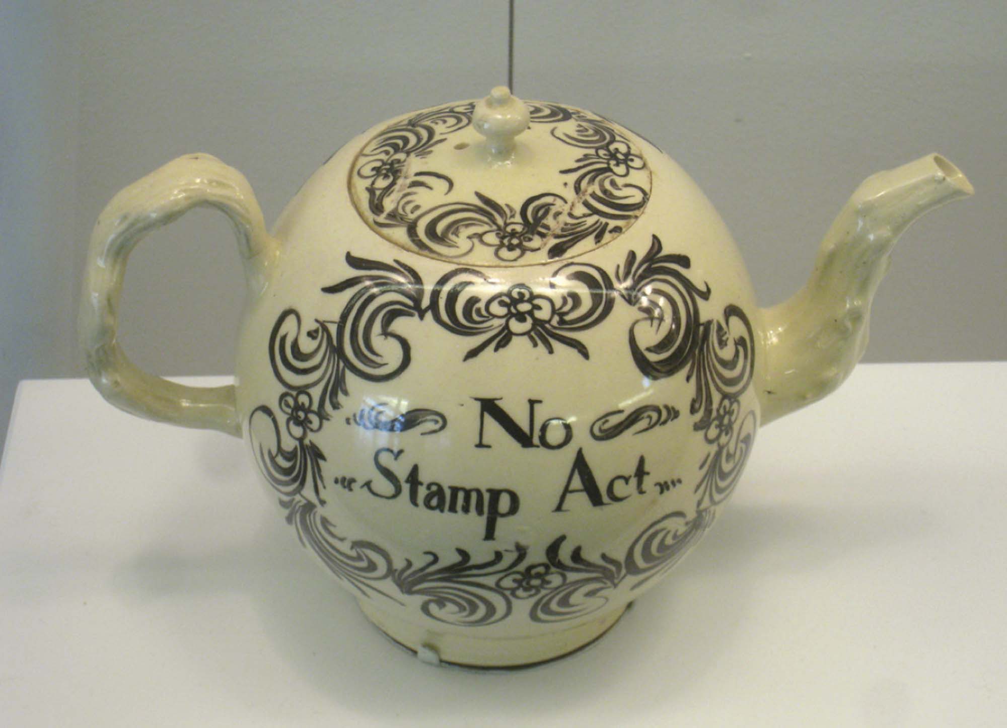 Photograph of a white teapot with black decoration and text reading “No Stamp Act”.