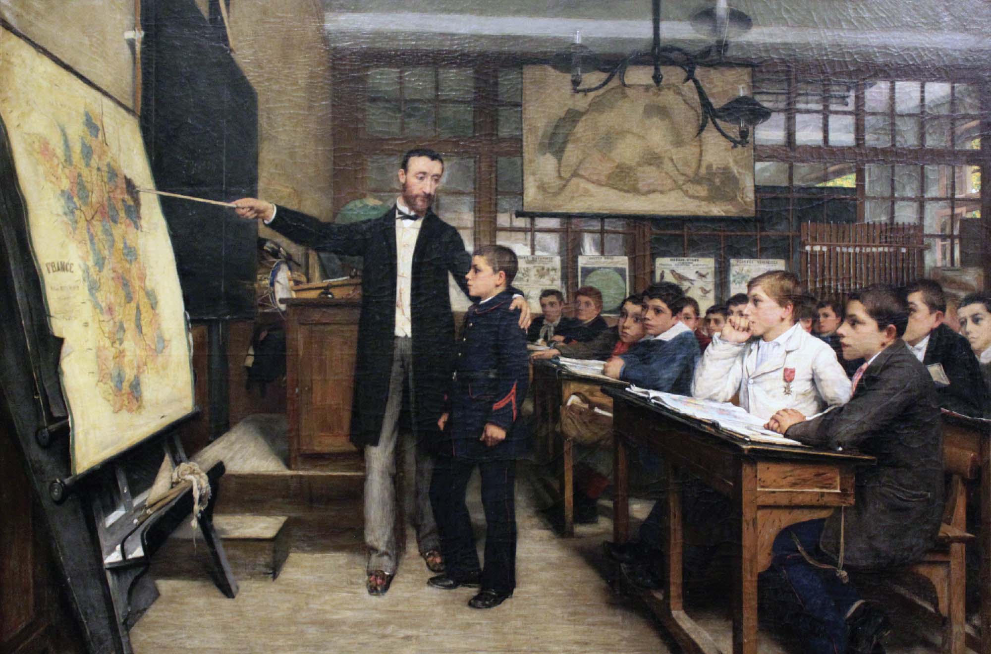 Painting of a class taking place in a classroom. Male students sit at wooden desks, and a teacher points at a large map at the front of the classroom.