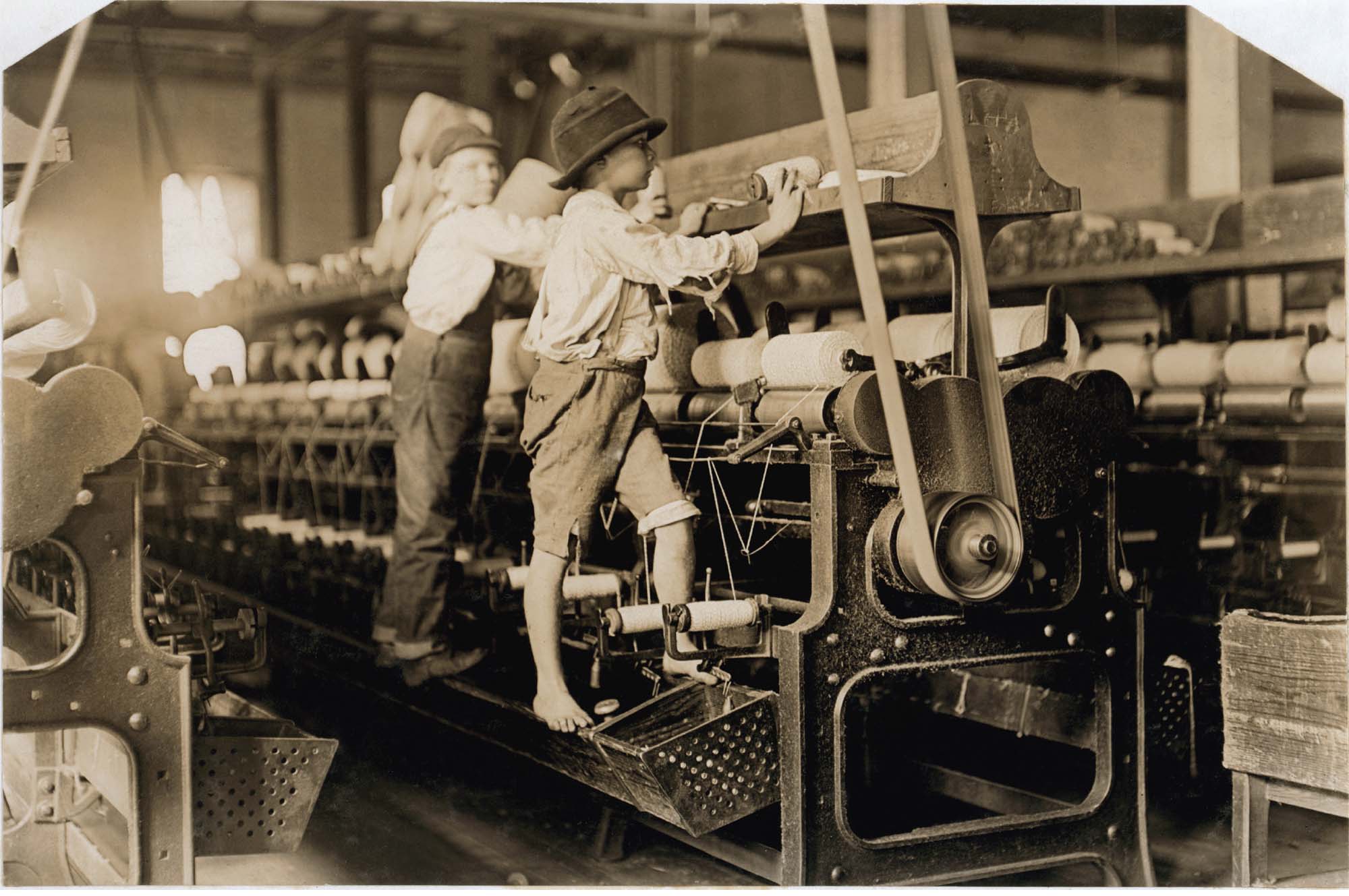 A black and white photo of small children, probably around the age of 8, operating large industrial machinery. One child has bare feet.