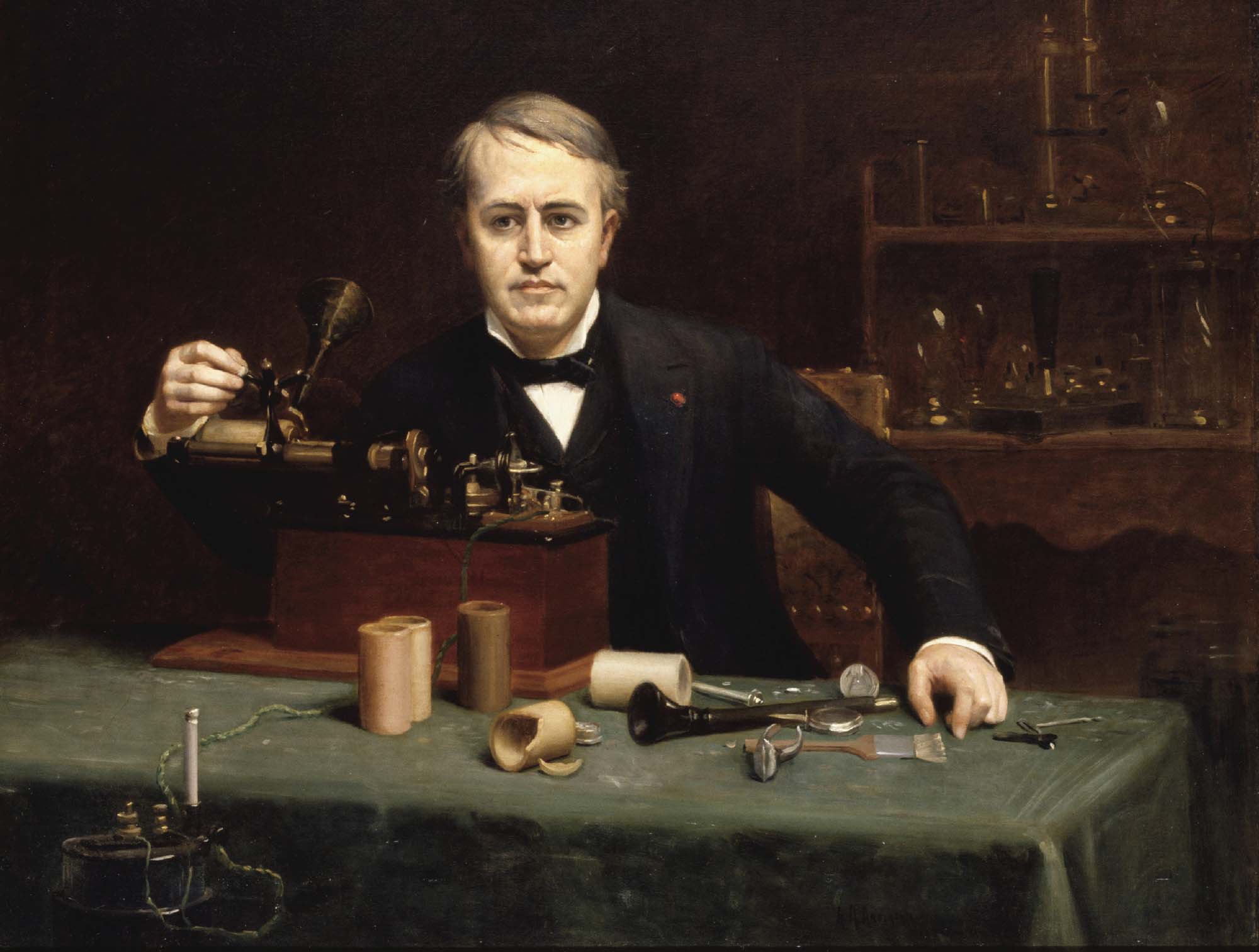 Portrait of a man in a suit working with a mechanical instrument at a desk littered with tools.