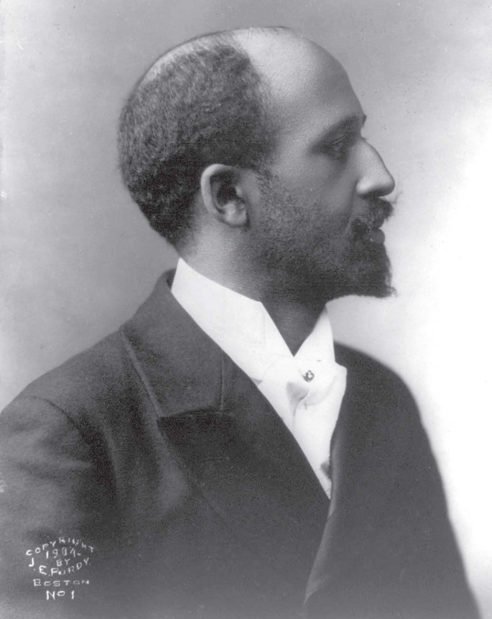 Photograph of W.E.B DuBois, taken of his profile. He is wearing a black jacket and white collared shirt.