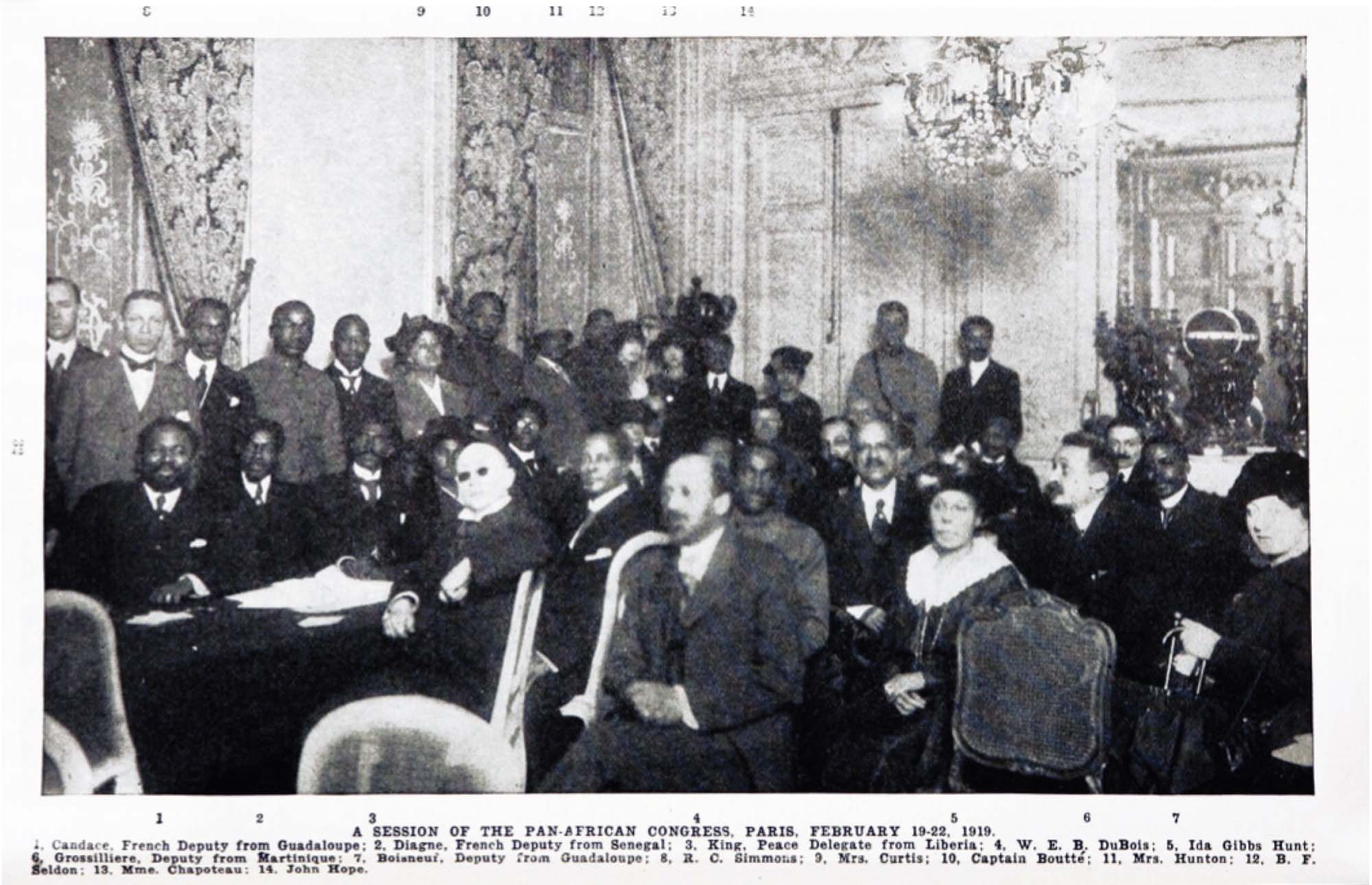 A photograph of a large group of people, mostly seated, in a meeting room. They are all facing in the same general direction, and some are smiling.