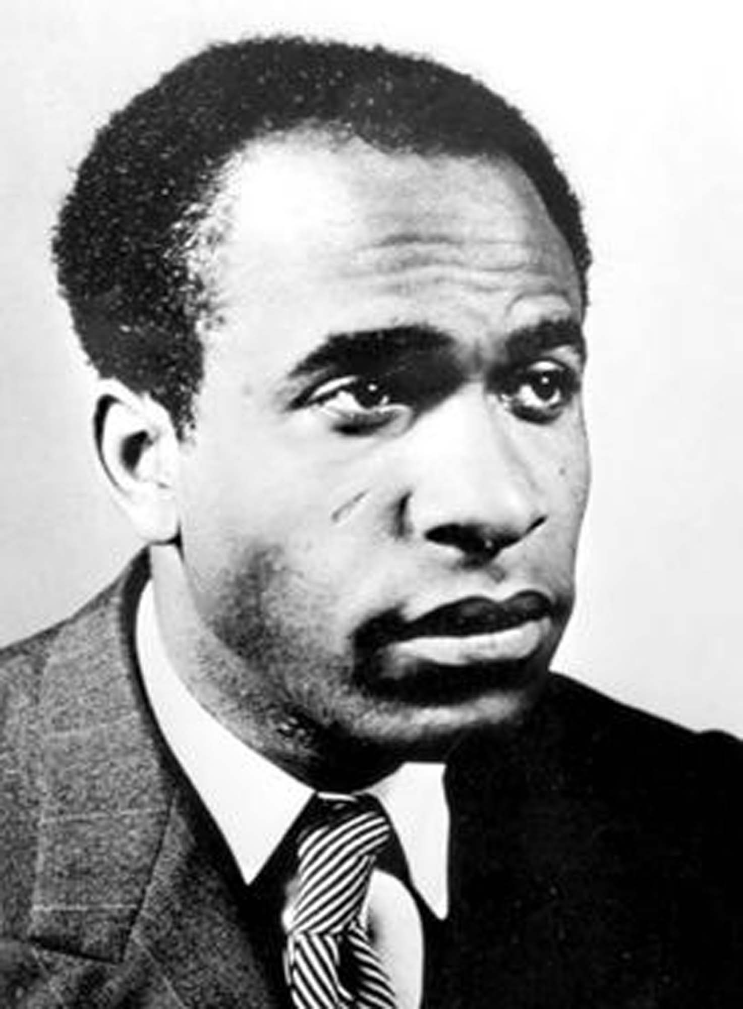 A portrait of French Caribbean psychologist Frantz Fanon. He is wearing a suit and tie and looking just past the camera.