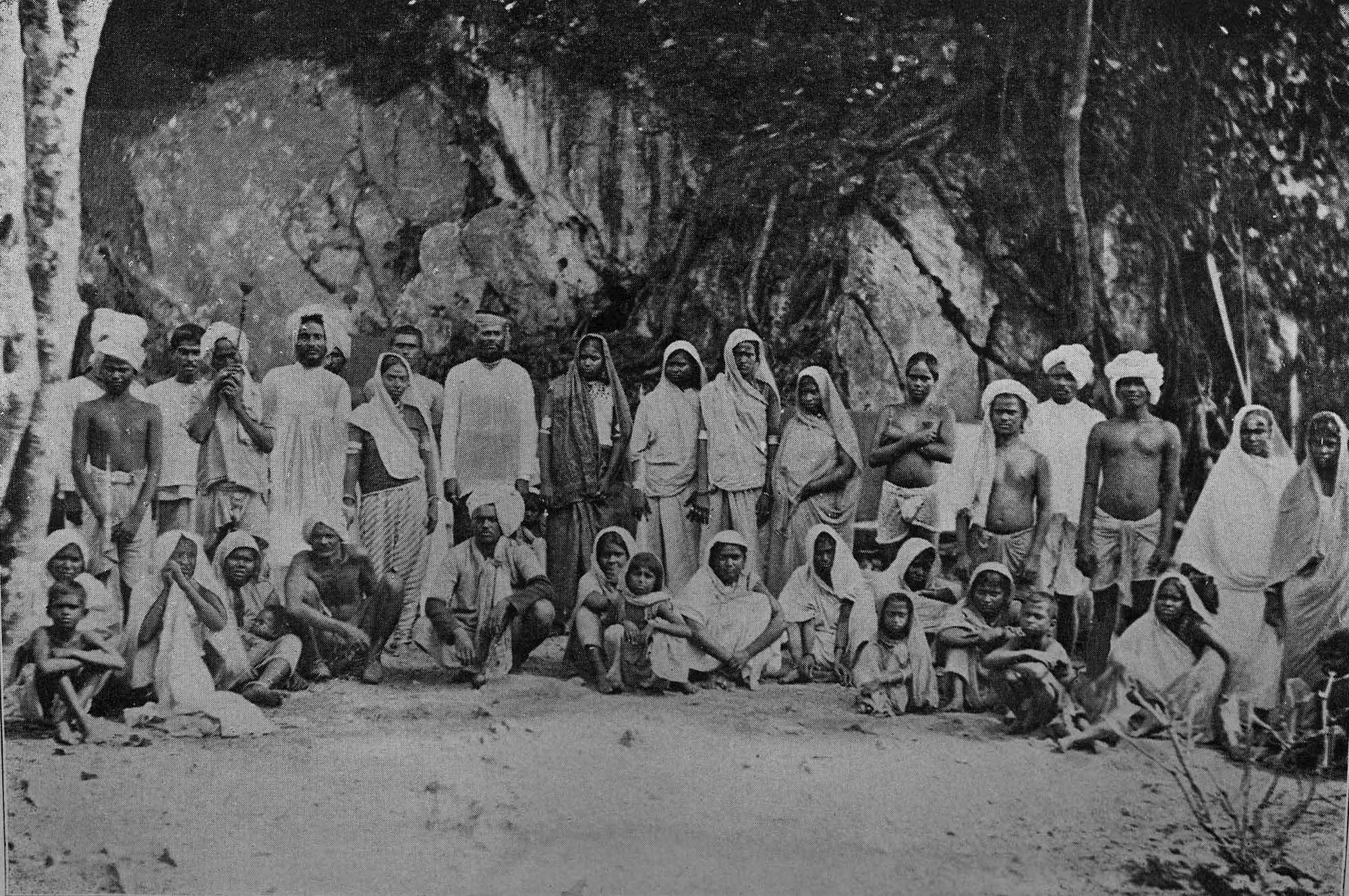 A photograph of colonized people, standing together outside, brought to the British West Indies to work as indentured laborers.
