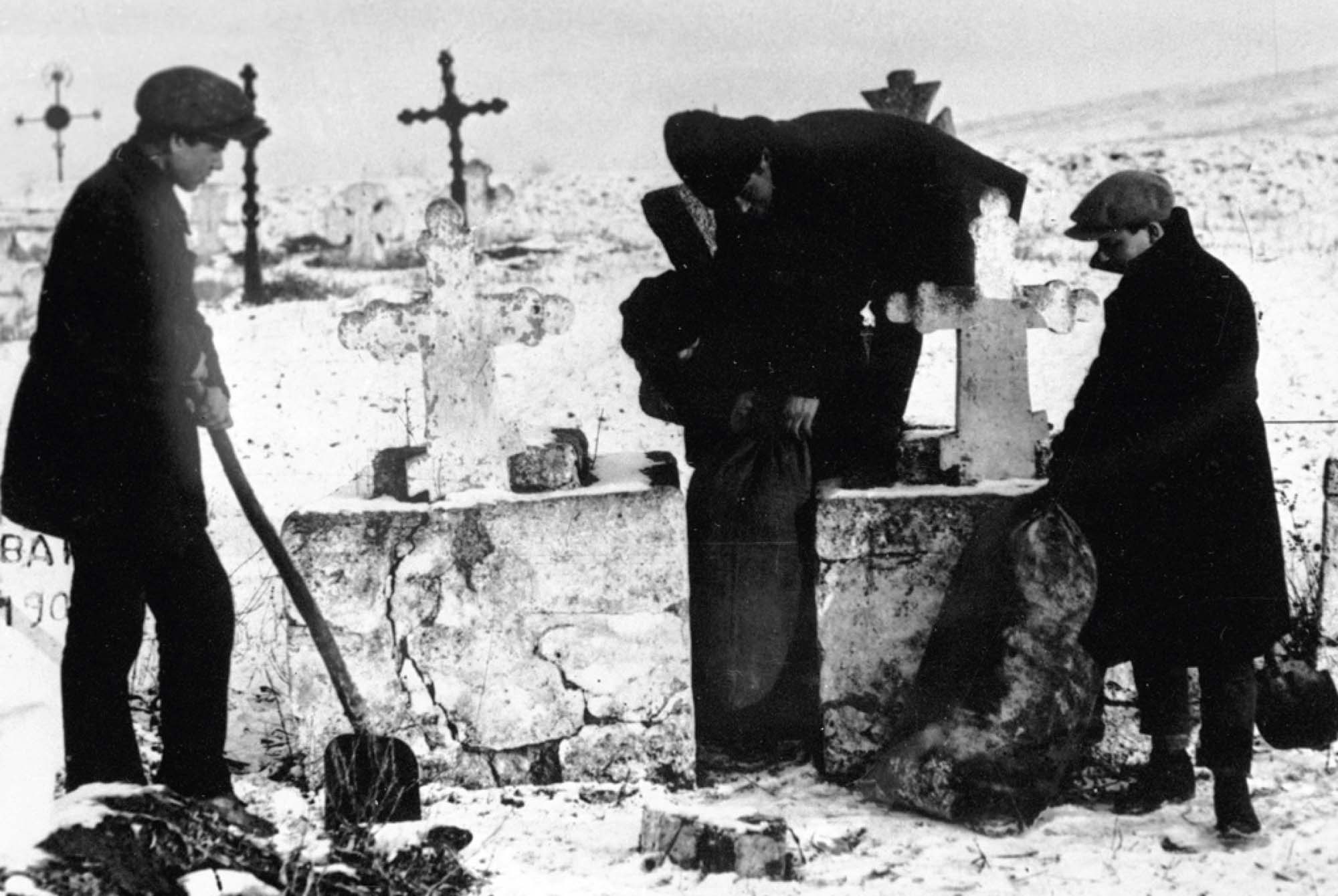Photo of Soviet agents with shovels next to a grave site. The agents are filling burlap sacks with grain that they seized from a Ukrainian peasant.