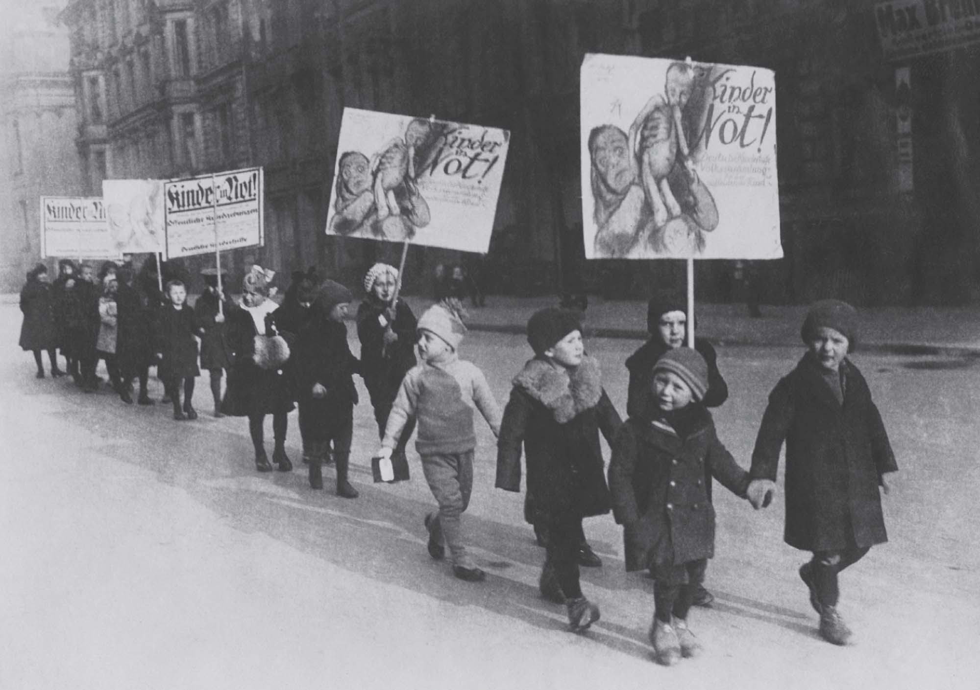Line of well-dressed children, some holding signs, protesting the plight of poor children in their city.
