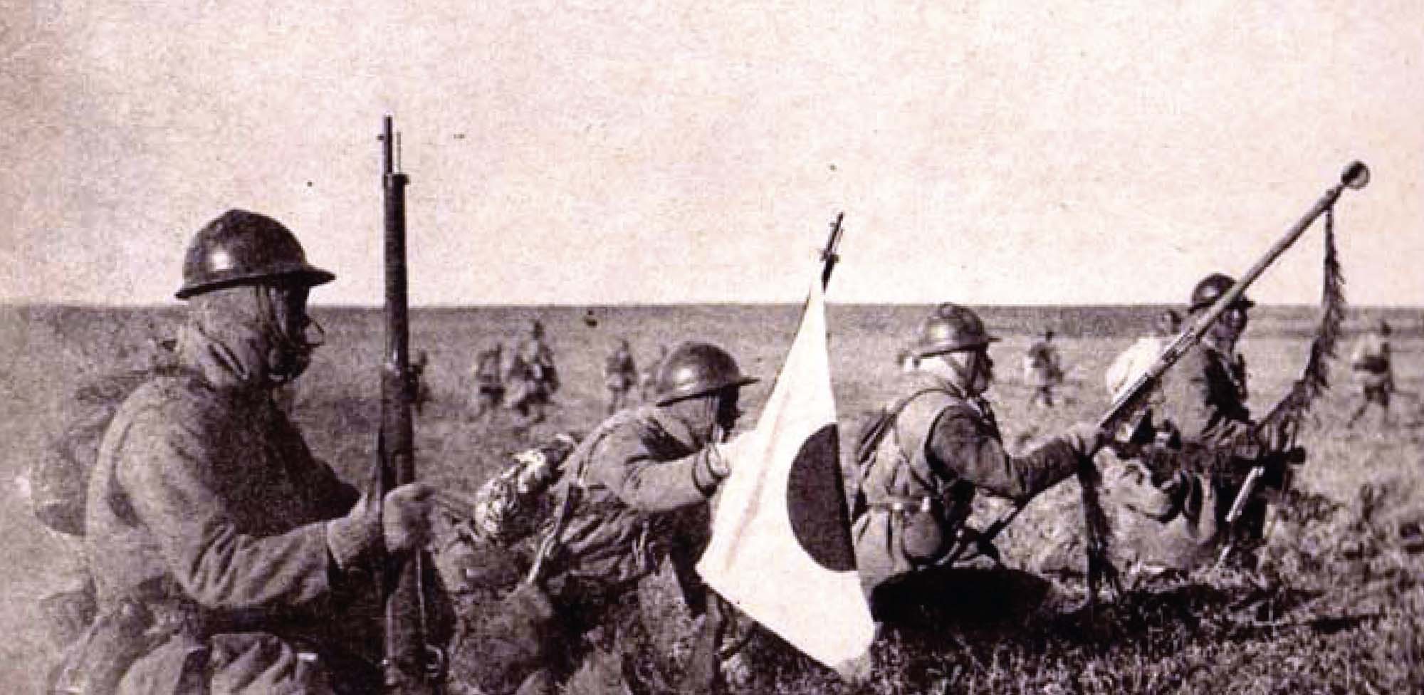 4 troops sit, kneeling, in an open field, holding rifles and a Japanese flag.