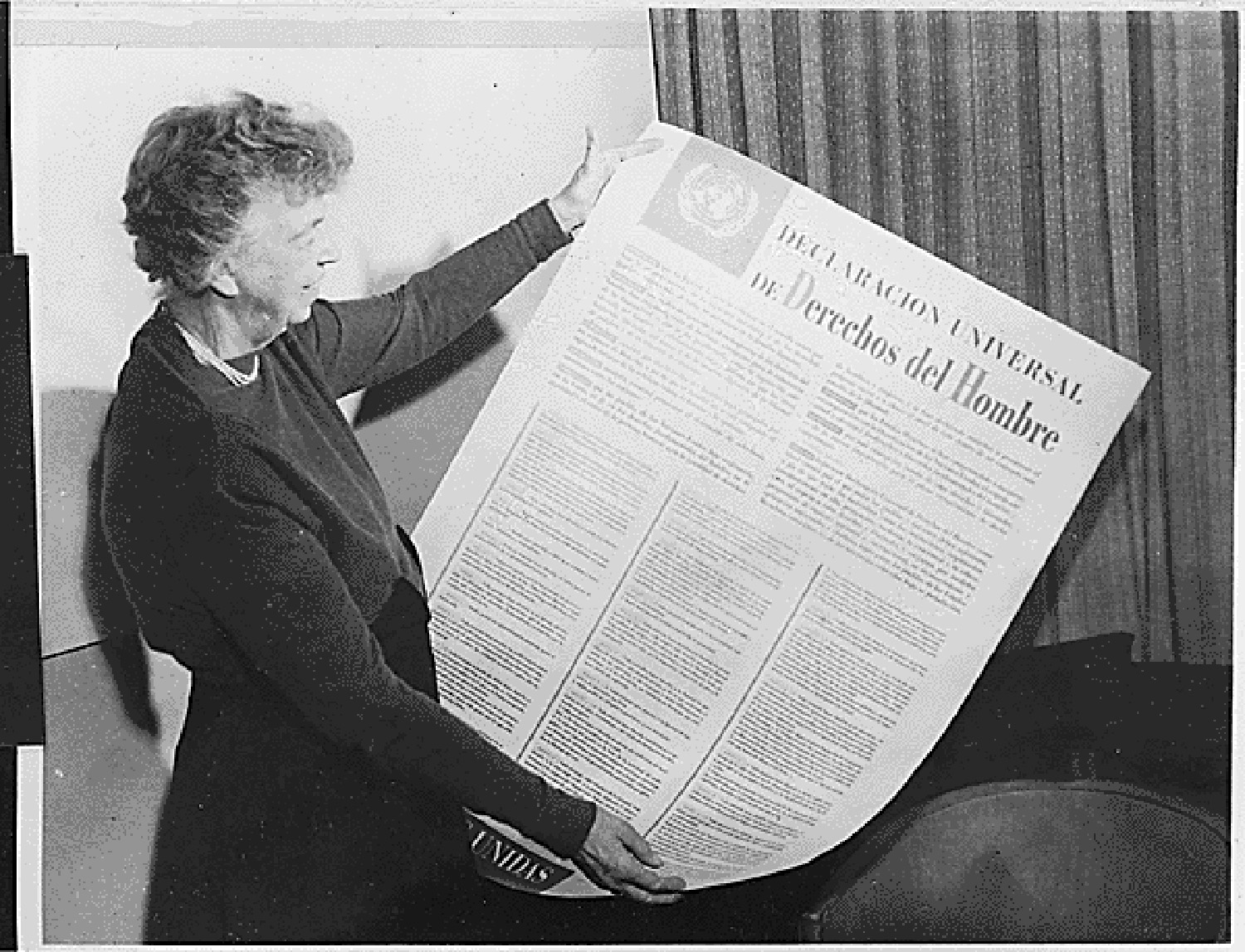 Photo of Eleanor Roosevelt holding a large sheet of paper that contains the Spanish version of the United Nations Universal Declaration of Human Rights.