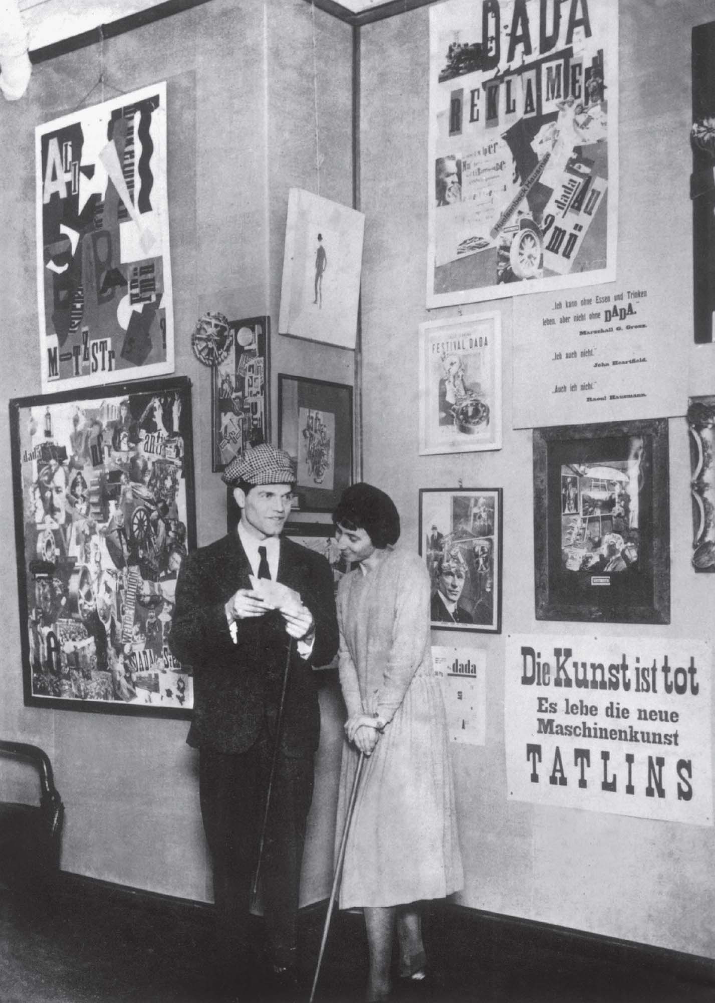 Dadaist artists Raoul Hausmann and Hannah Hoch standing in front of a wall with posters at the Dada fair in Berlin.