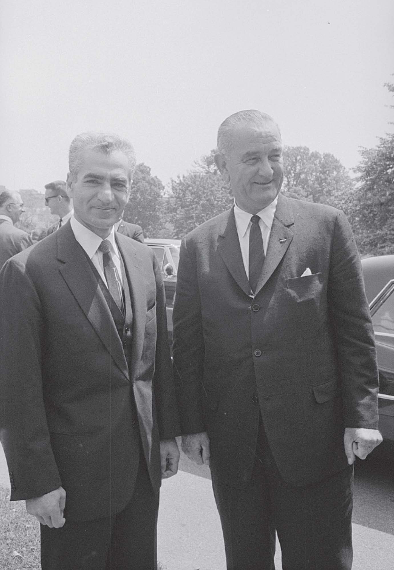 A picture of two, smiling men, standing next to one another. Both are dressed in suits and ties.