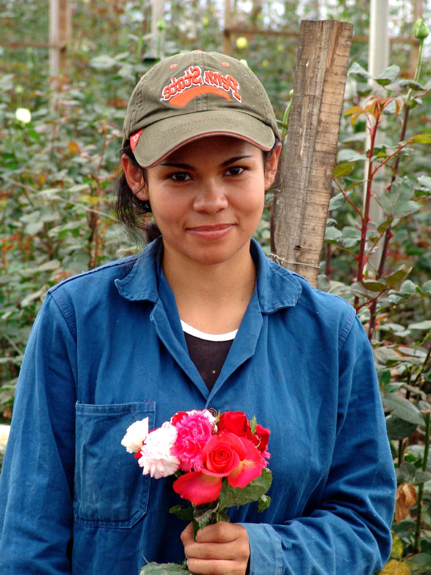 A young woman, dressed in a ballcap and work shirt holds a bouquet of roses.