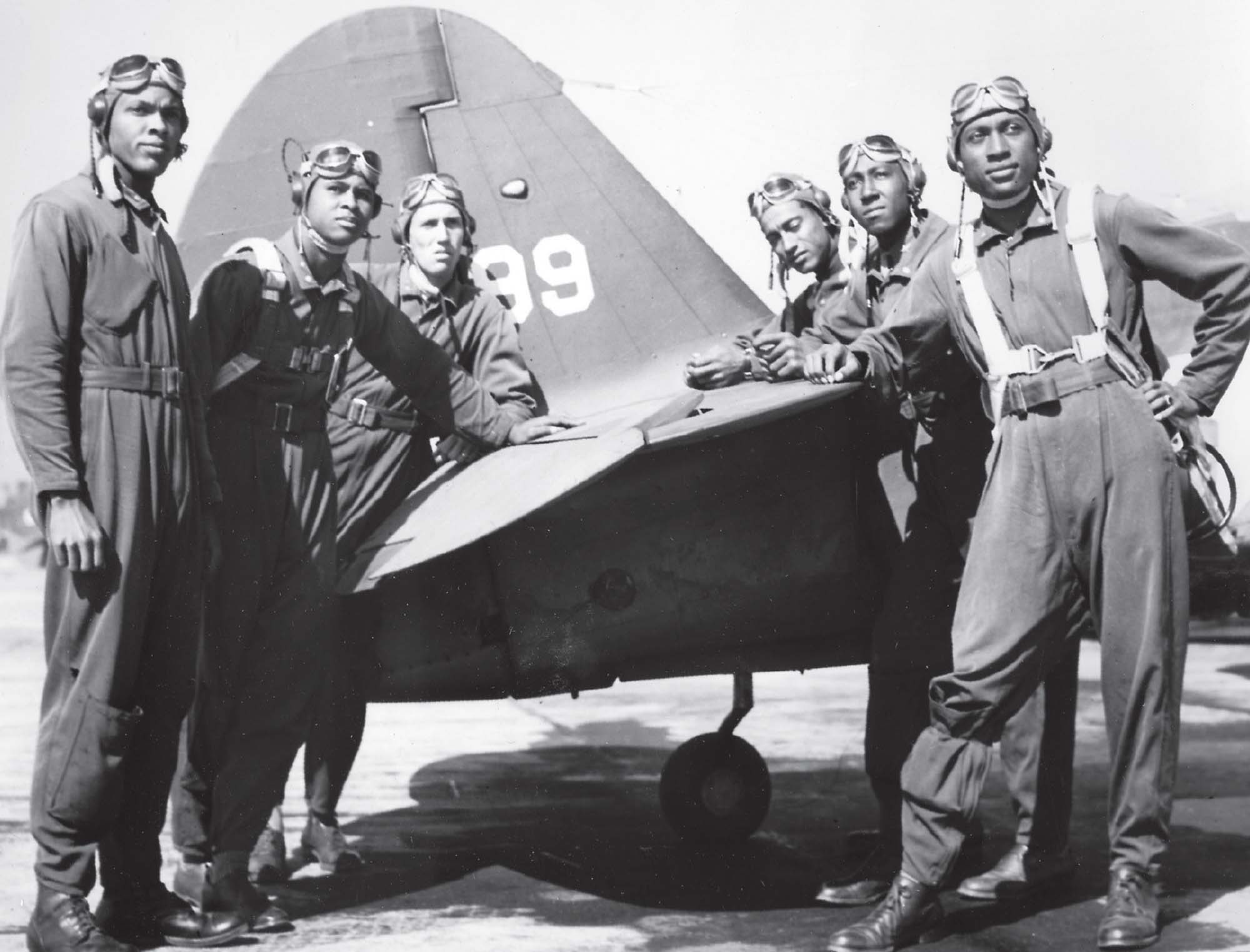 Black and white photo of six African-American men in aviation gear posed around a World War II aircraft.