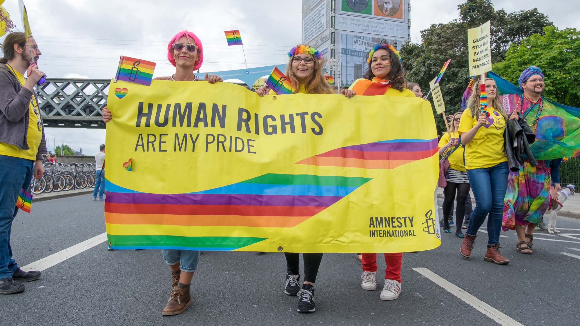 Photo of protestors with Amnesty International marching at the 2016 Pride parade in Ireland. They are holding a yellow banner that says “Human Rights Are My Pride”.
