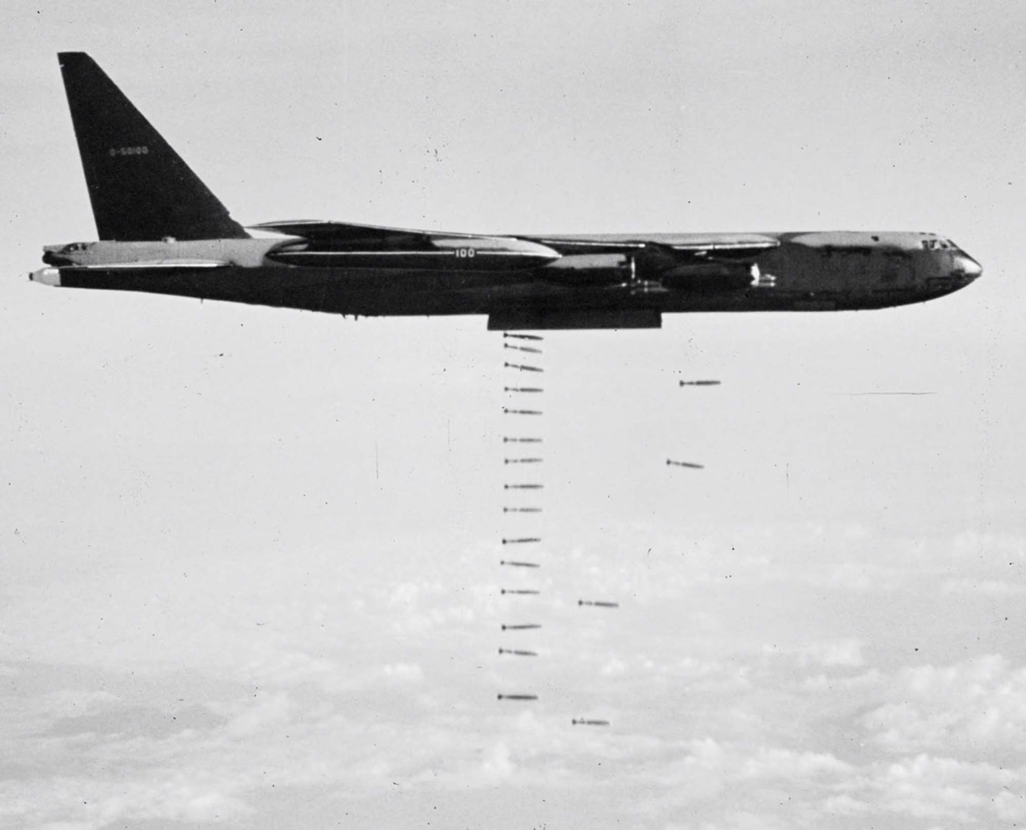 An airplane, flying above the clouds, drops a line of arrow-shaped bombs.