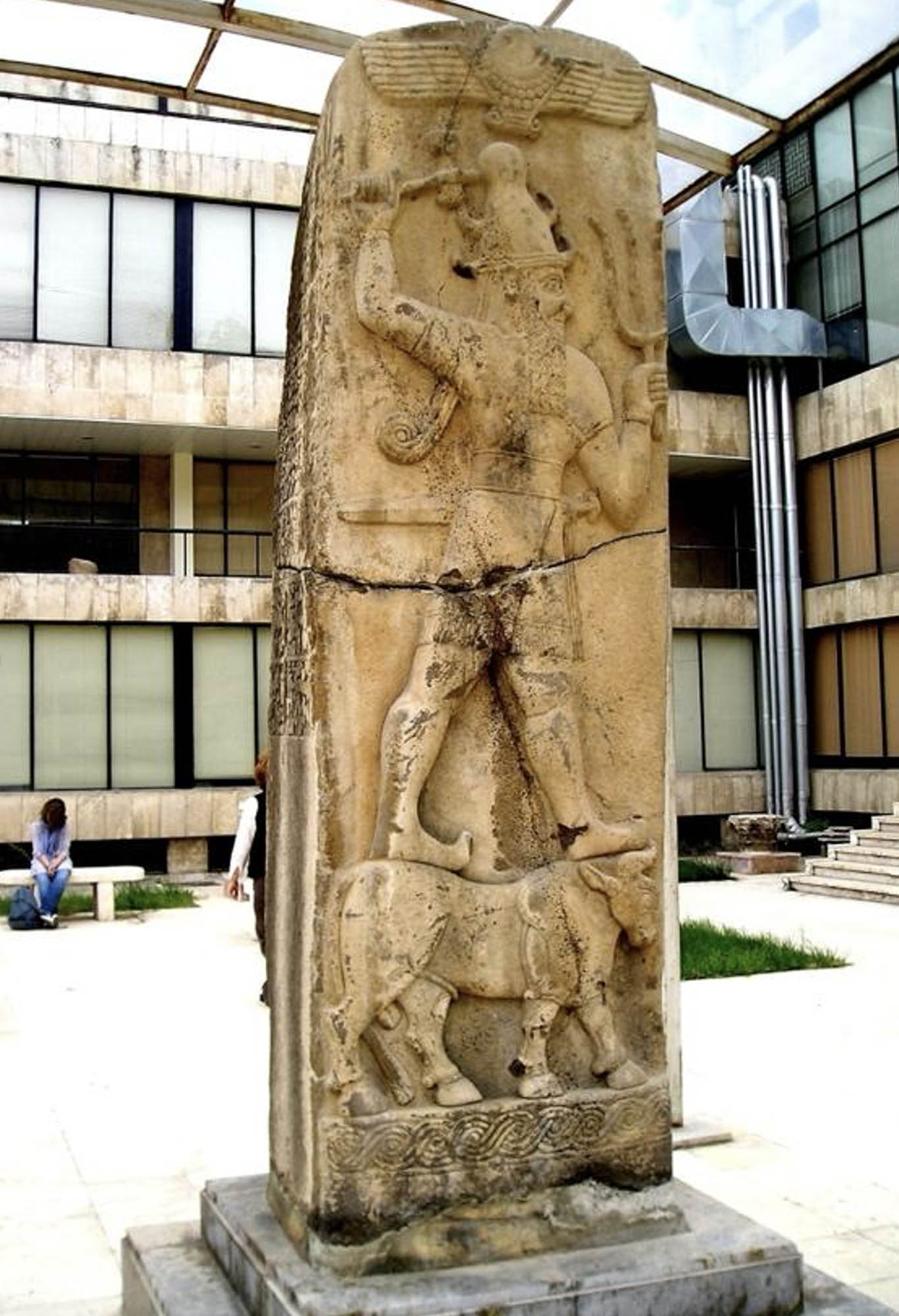 Large, standing stone sculpture with a carved figure standing on a bull.