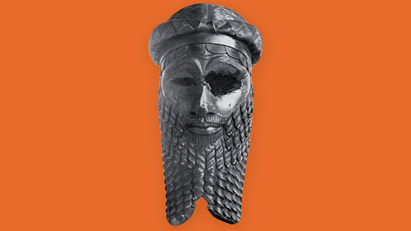 Bronze sculpted head of an Akkadian emperor featuring a very detailed carved beard and hat. One eye is missing from the sculpture, probably a result of age decay.