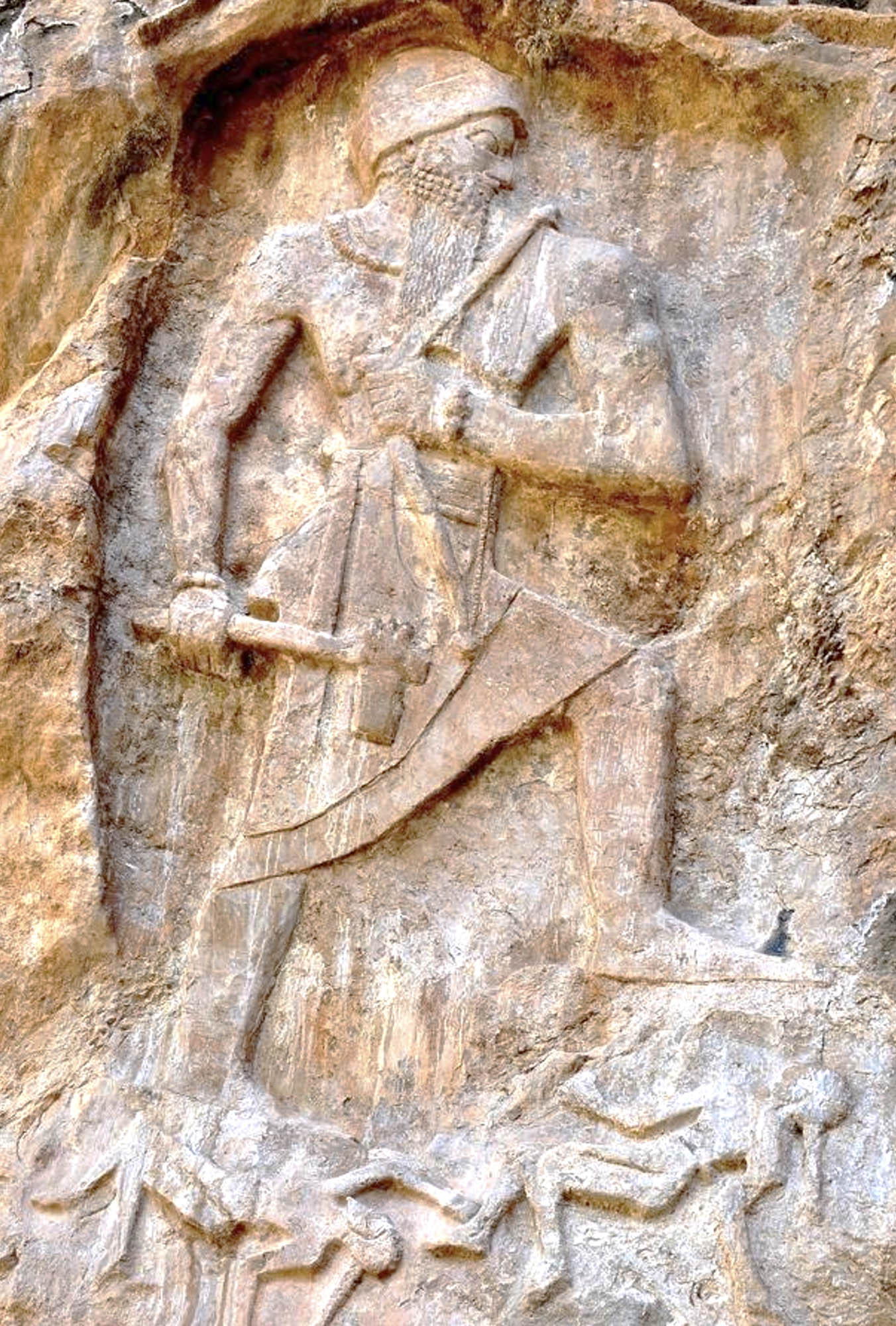 Carved rock depiction of a very large man stomping on much smaller people.