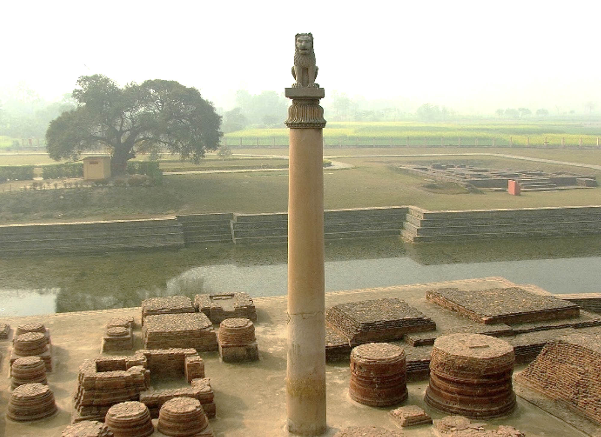 A site of ruins in India. A pillar in the foreground is topped by a seated lion.