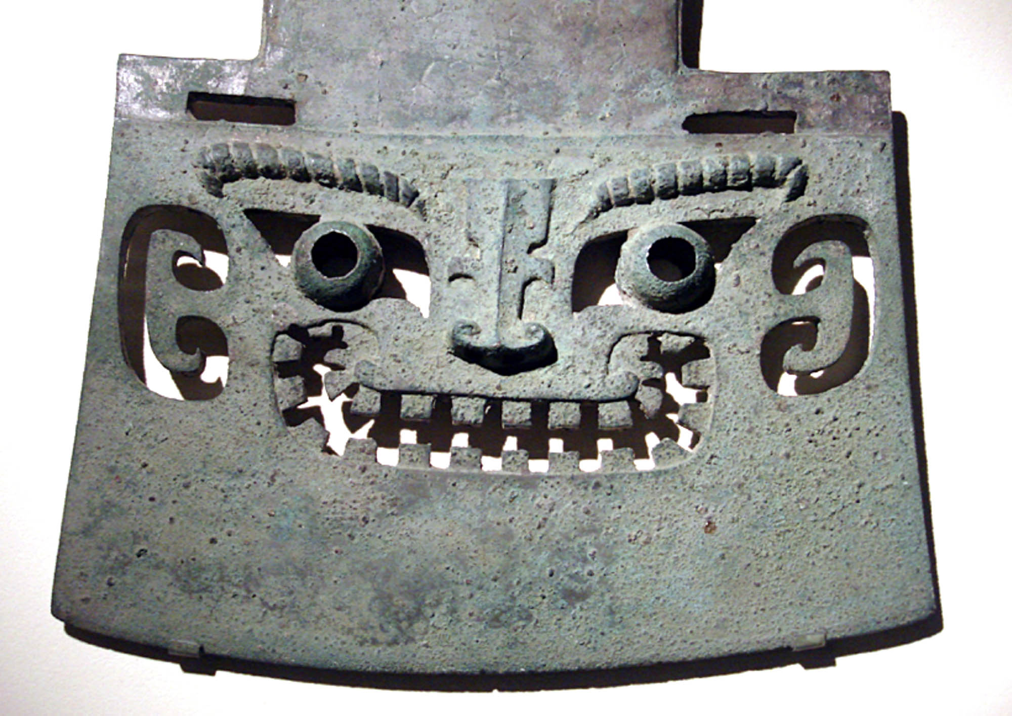 Photo of a piece of artwork: a face is carved into a bronze axe.