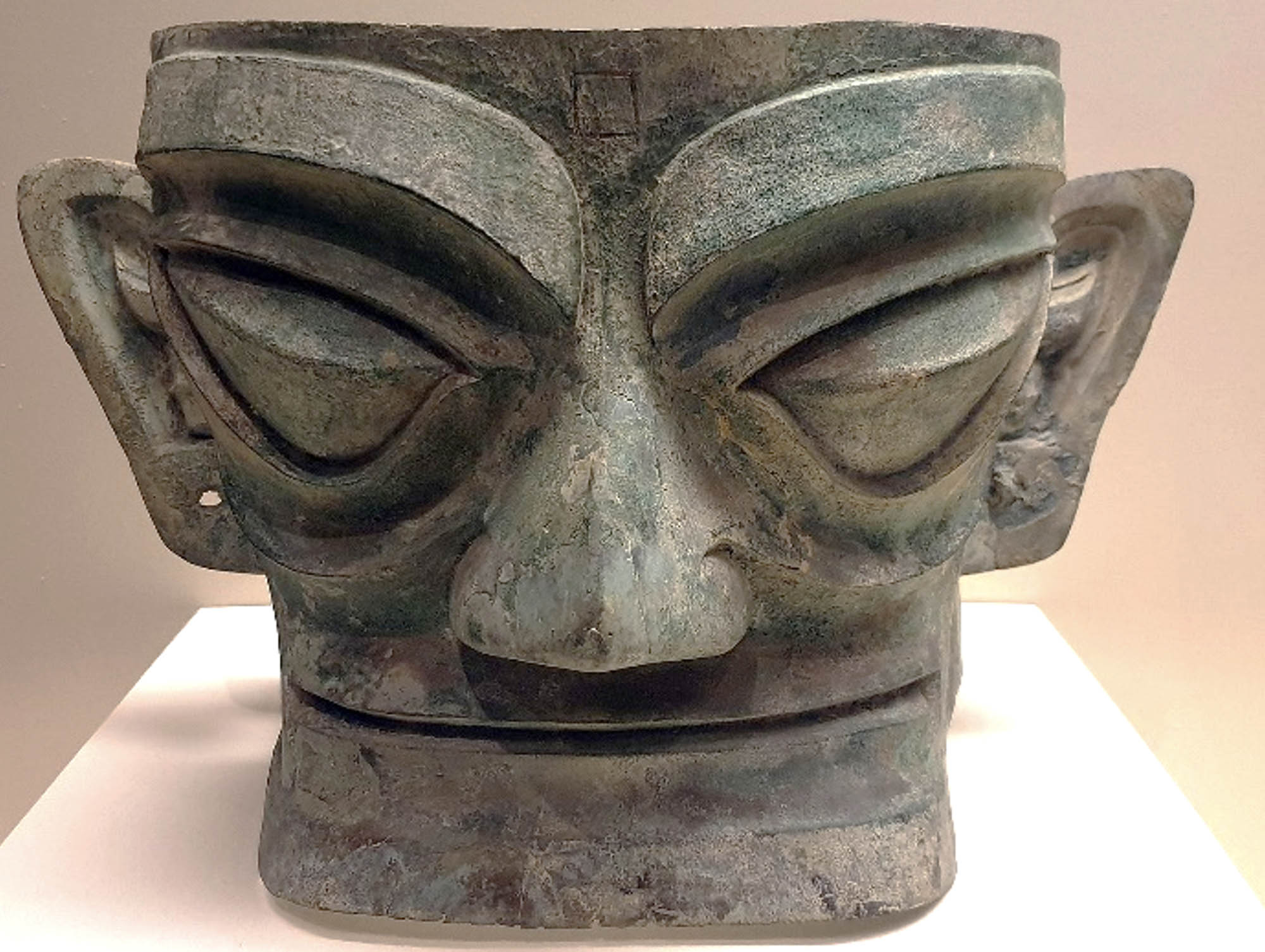 Bronze mask of bold design with exaggerated, large eyes, nose, mouth, and ears.