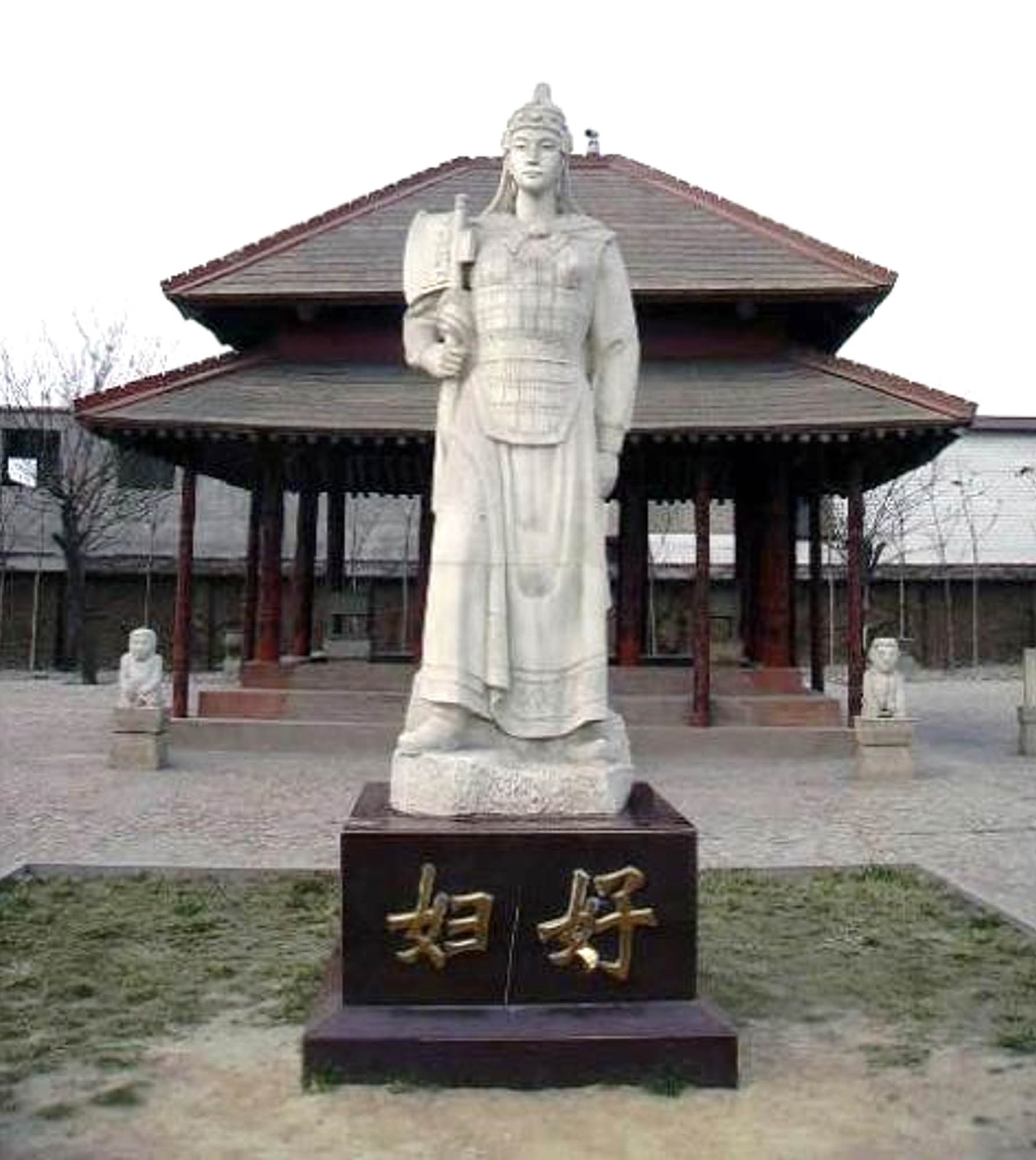 Modern day photograph of a detailed statue in front of a temple. The statue stands tall, holding a large axe at one side and wearing ornate clothing.