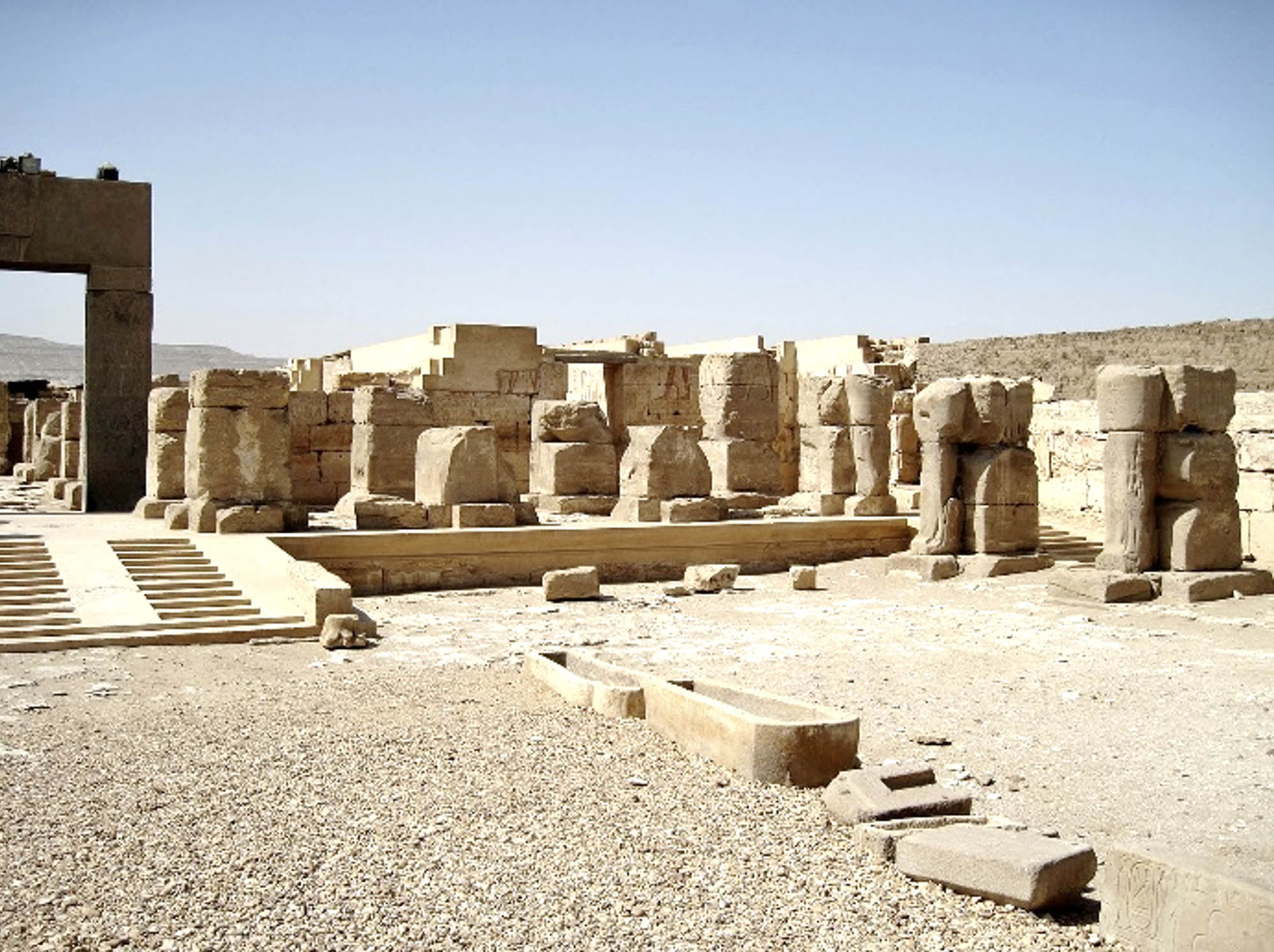 Stone ruins in the desert. In the middleground is an arch, in the background are walls and columns.