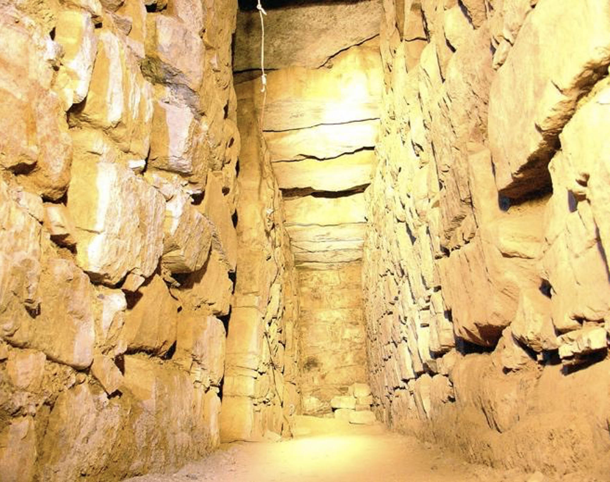 A photograph of an interior hallway featuring large stone walls and ceiling