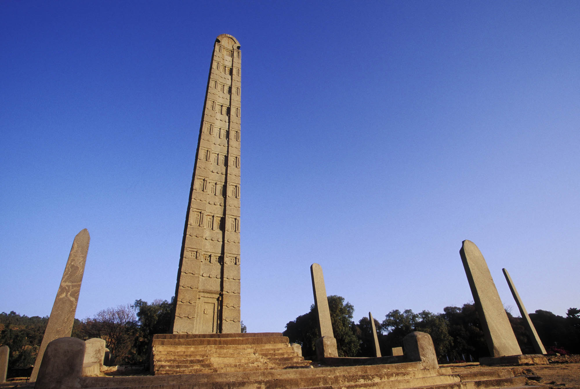 Photograph of several tall, pointed stone slabs. One, in the center, rests on a staircase and is carved with symbols