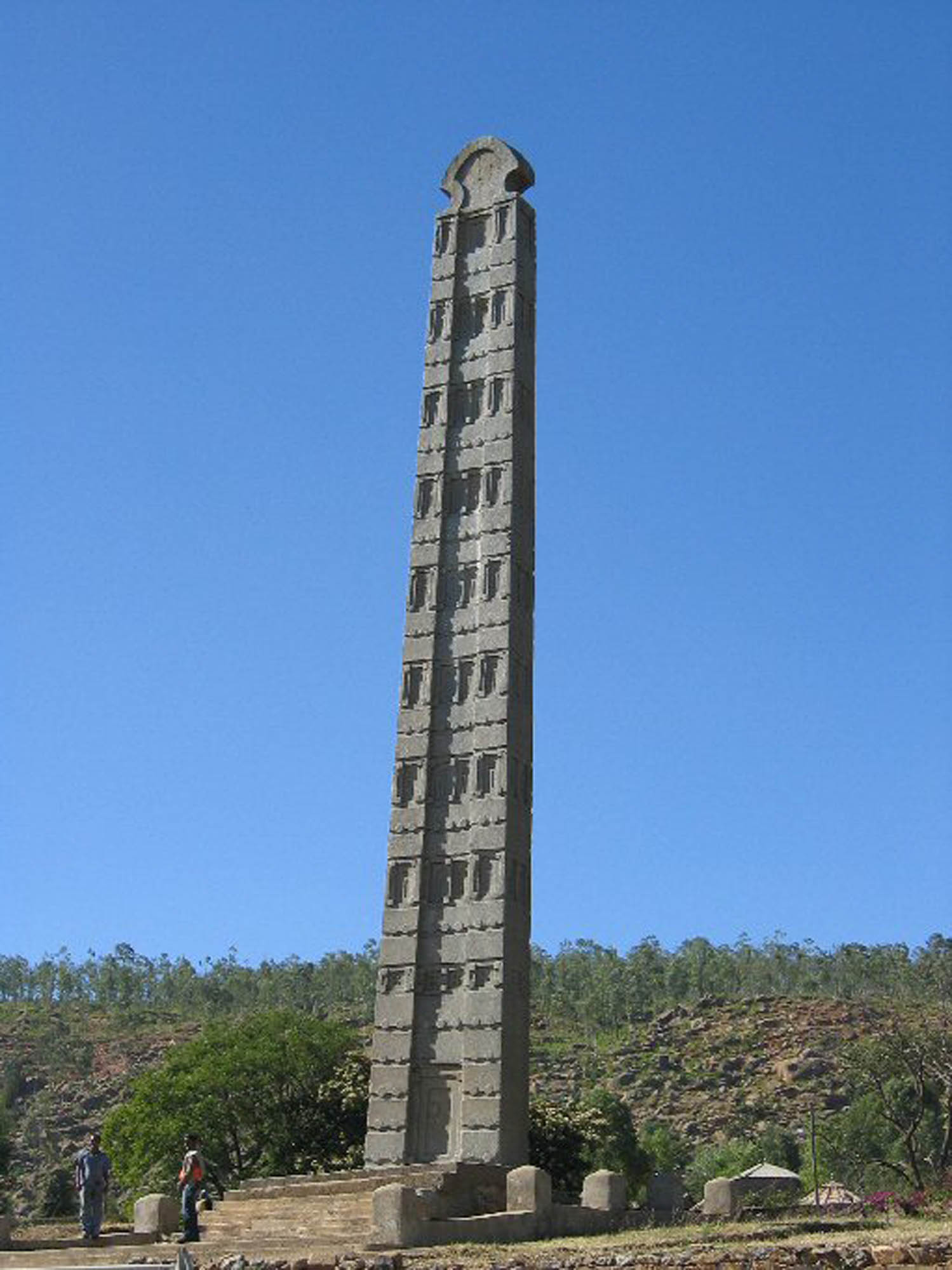 A tall, pointed stone slab is carved with symbols and rests on a staircase.