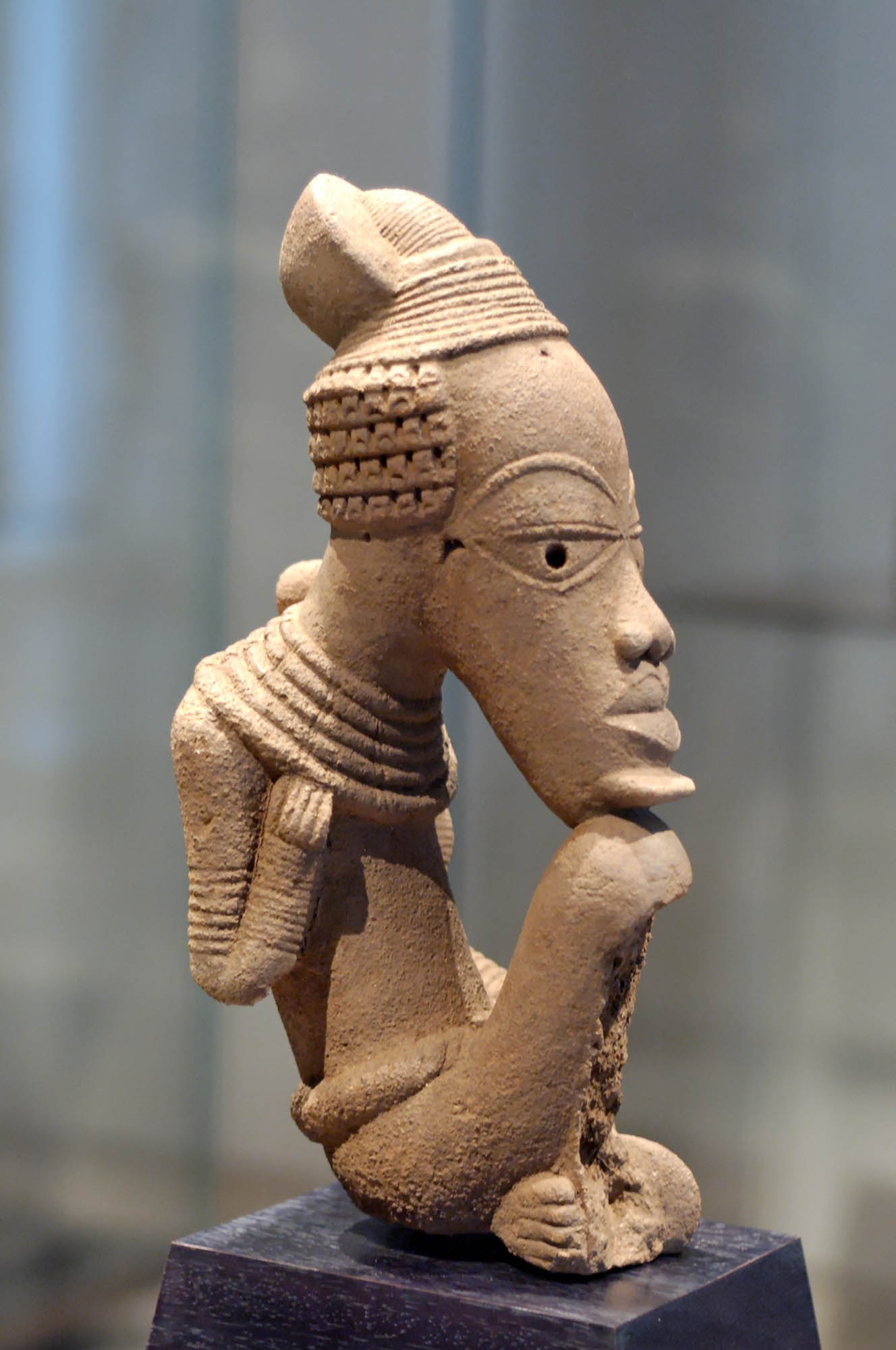 Sculpture of a figure with an elongated face in a seated position
