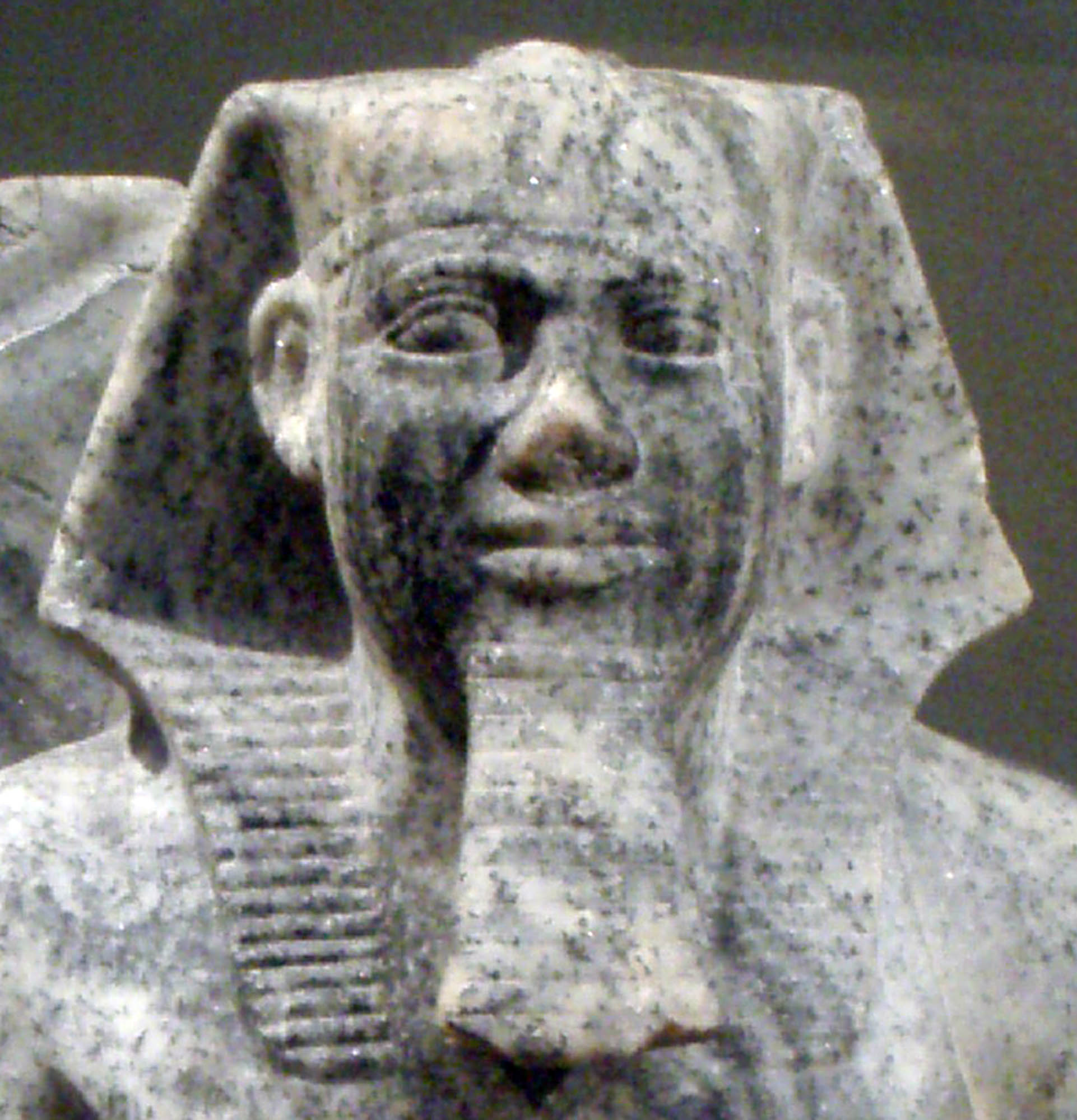 A picture of a sculpture of a Pharoah made of a marbled stone. The face is detailed, and the sculpture wears a headdress.