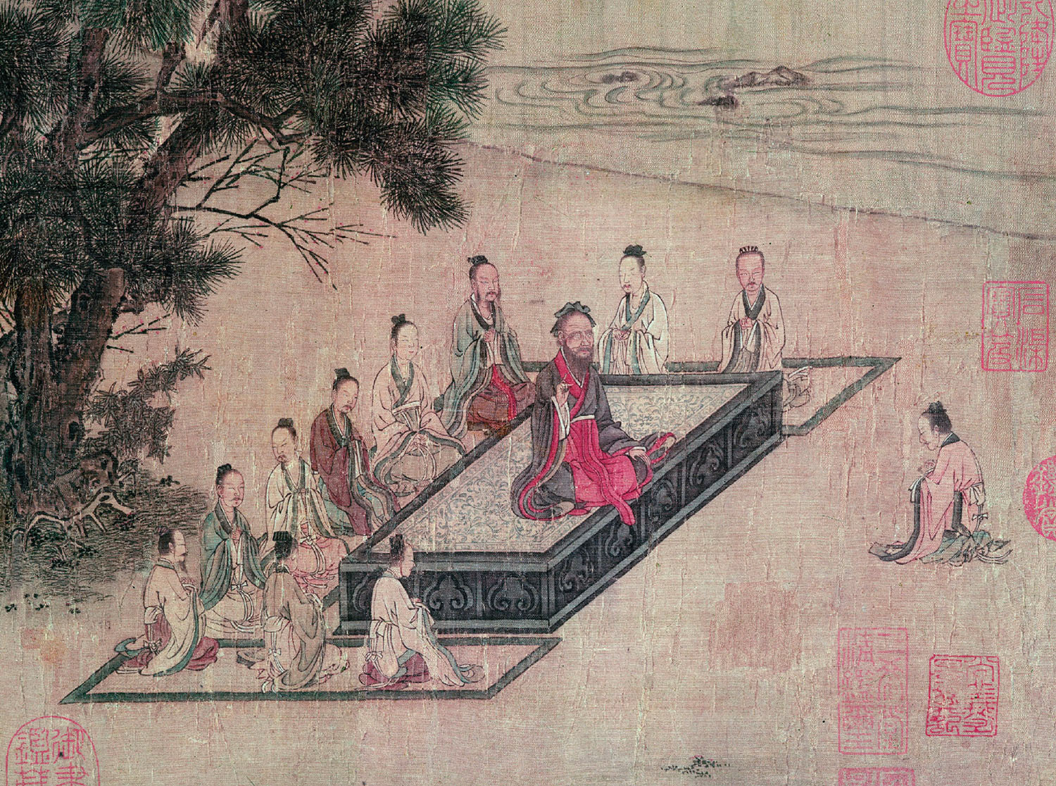 Tapestry painting shows several people sitting cross-legged on the ground, surrounding a pedestal. On the pedestal is another seated person, and he is lecturing the others.